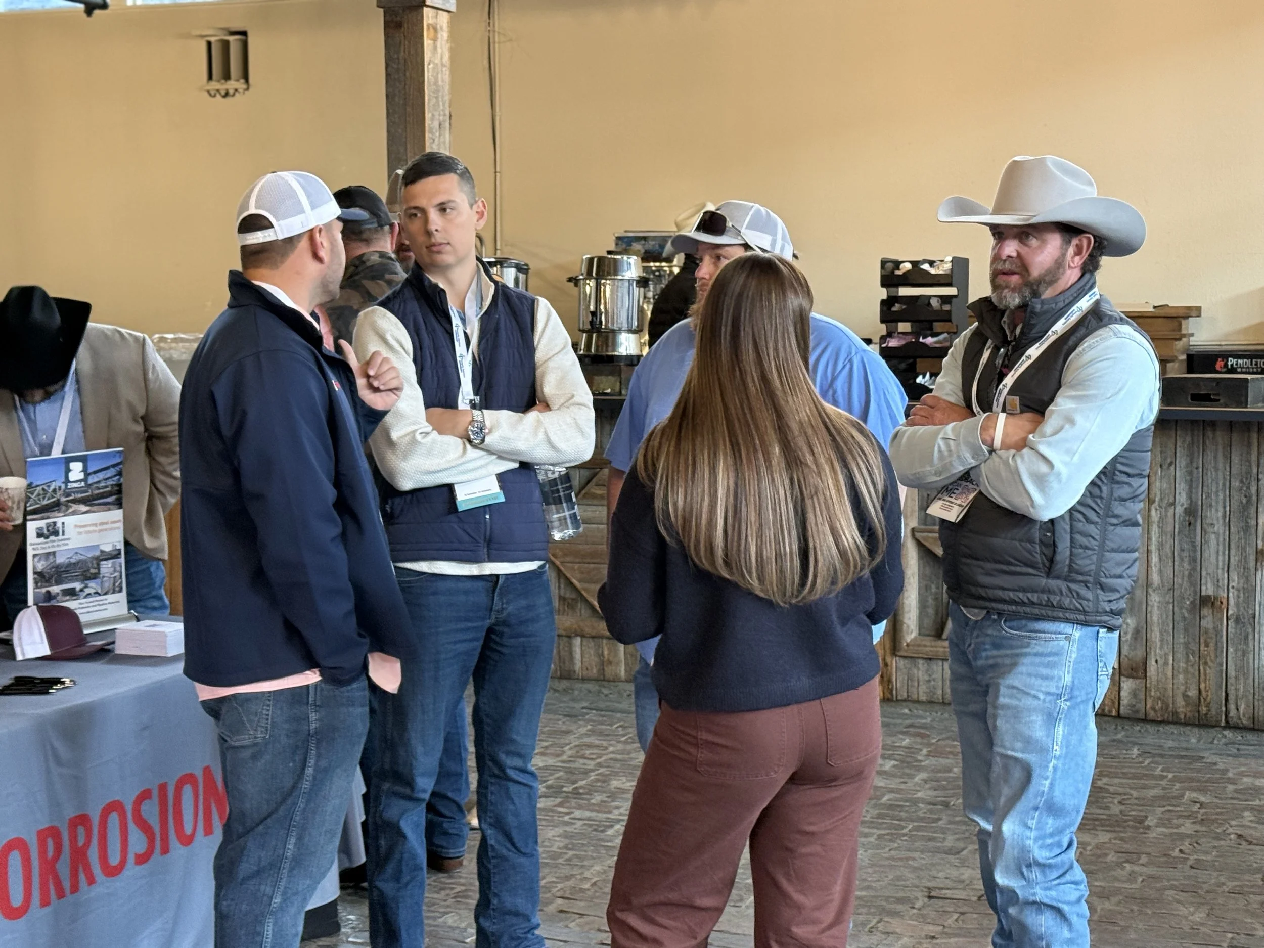 Group of five people in casual and western attire standing together and talking at an indoor event.
