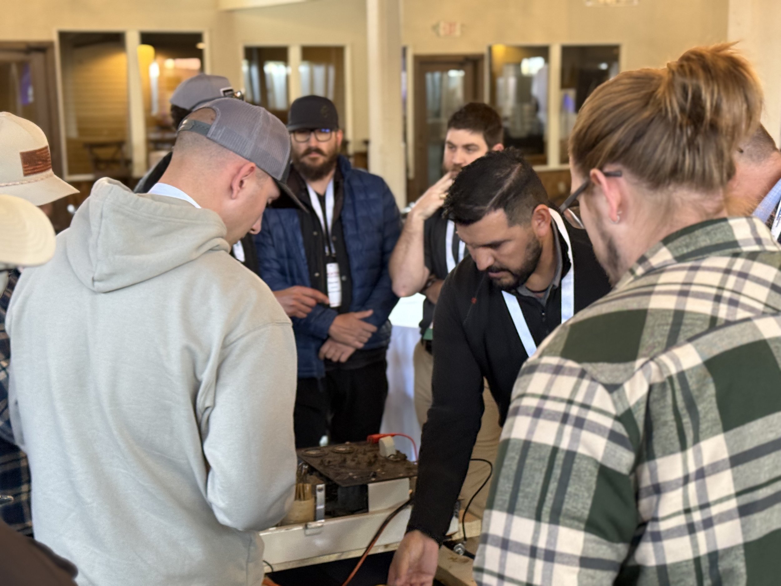 Group of people gathered around a table examining electronic equipment.
