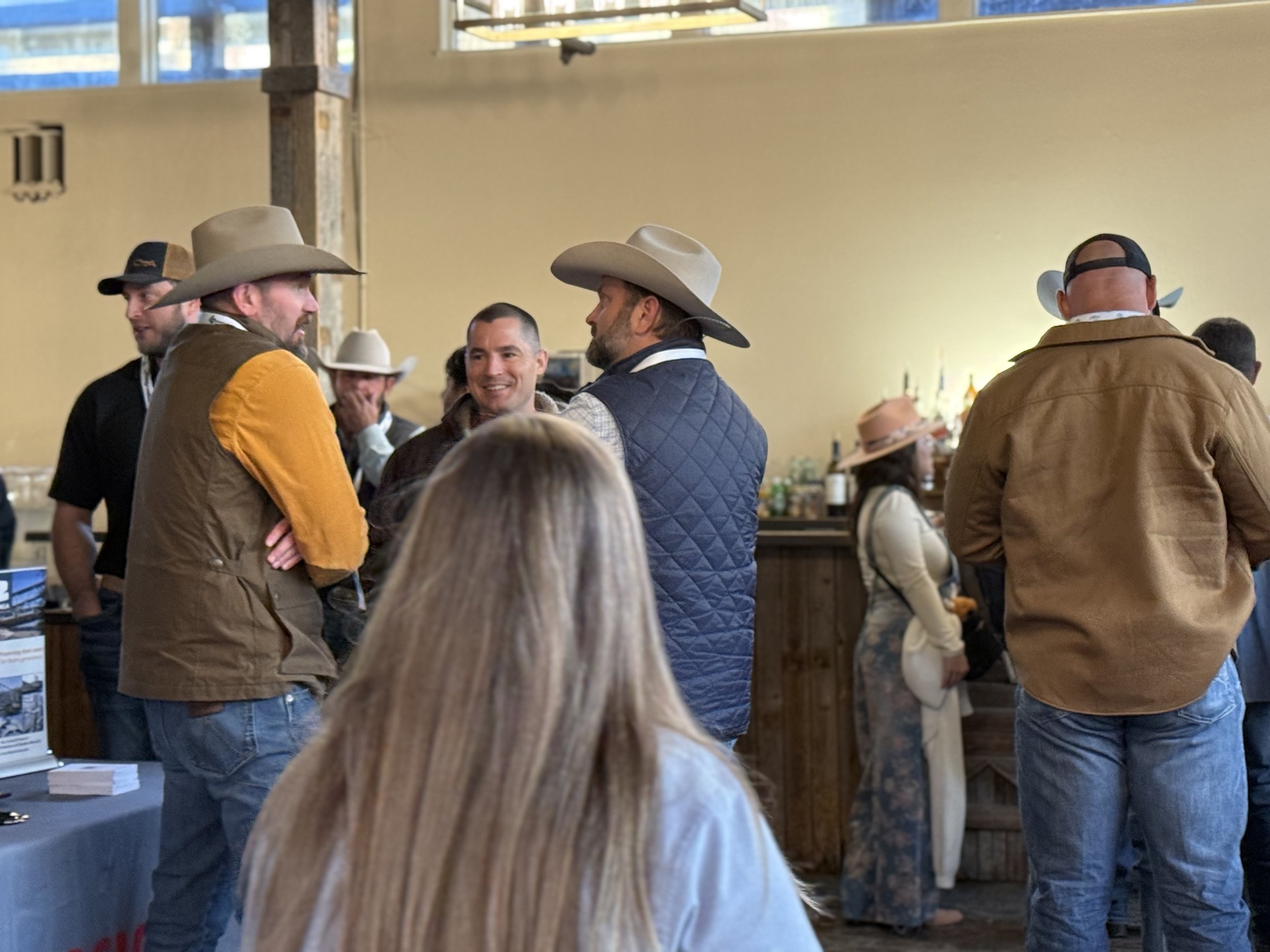 People at a social gathering wearing cowboy hats, some in brown and others in beige, with a bar in the background.