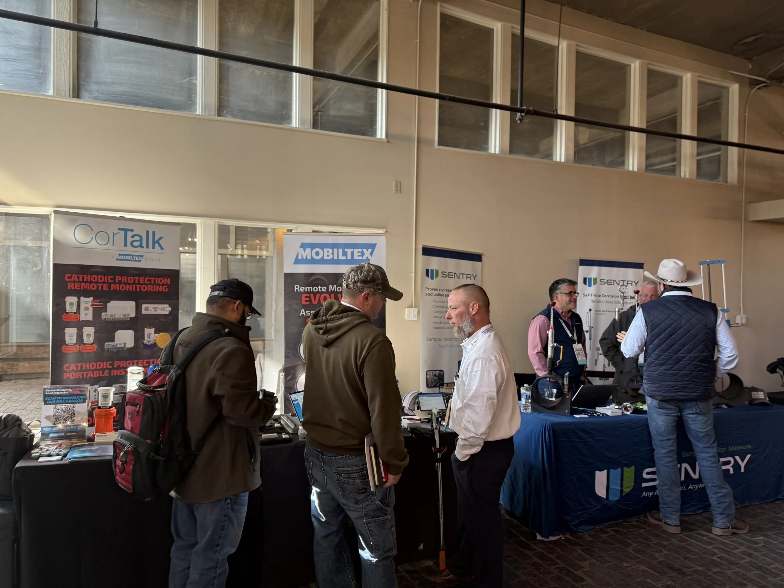 People attending a technology trade show or conference, standing around booths with banners and product displays for COR Talk, MOBITEX, and SENTRY.