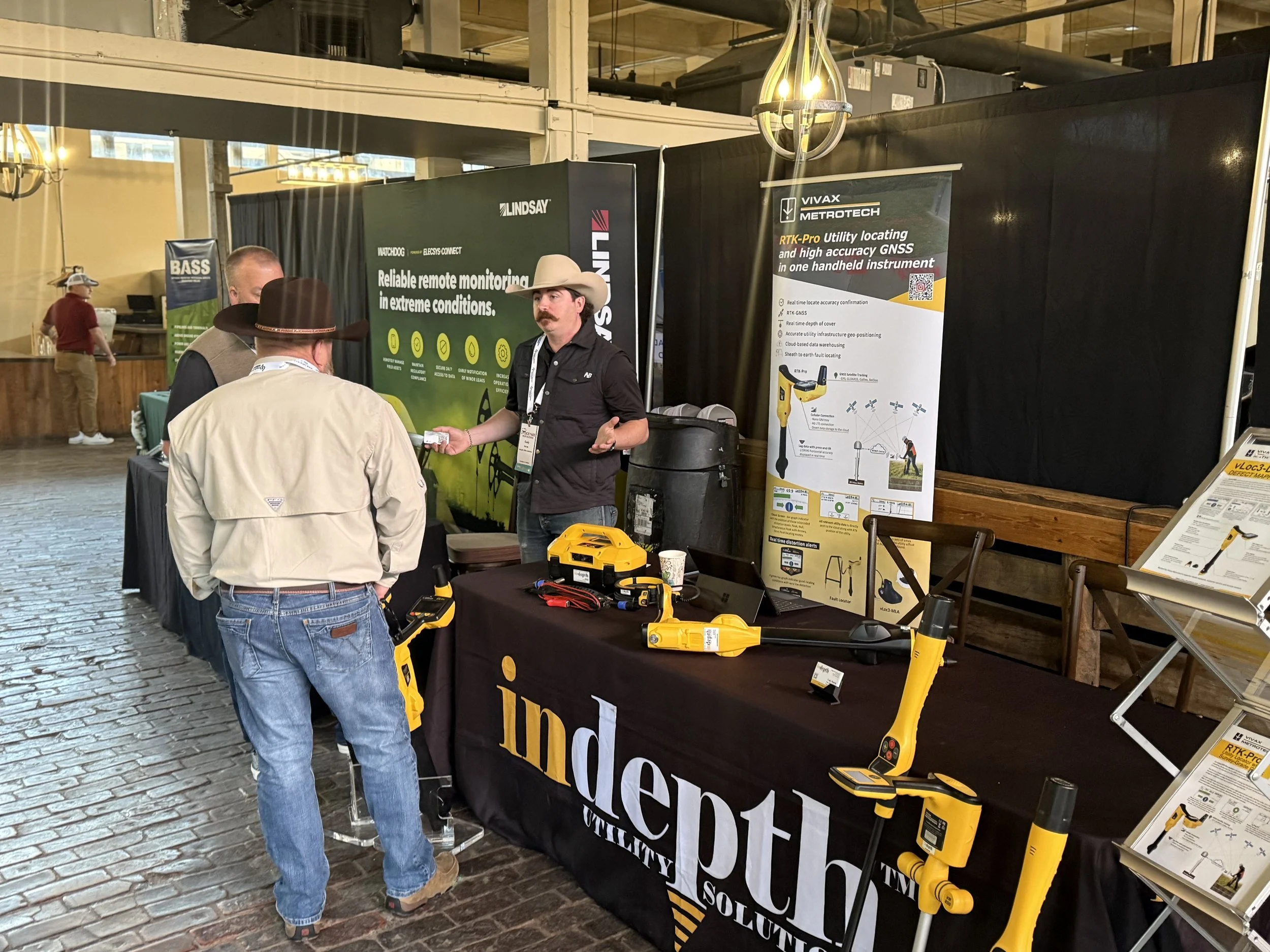 Trade show booth for independent utility solutions featuring tools and equipment, with two men in cowboy hats talking to a representative.
