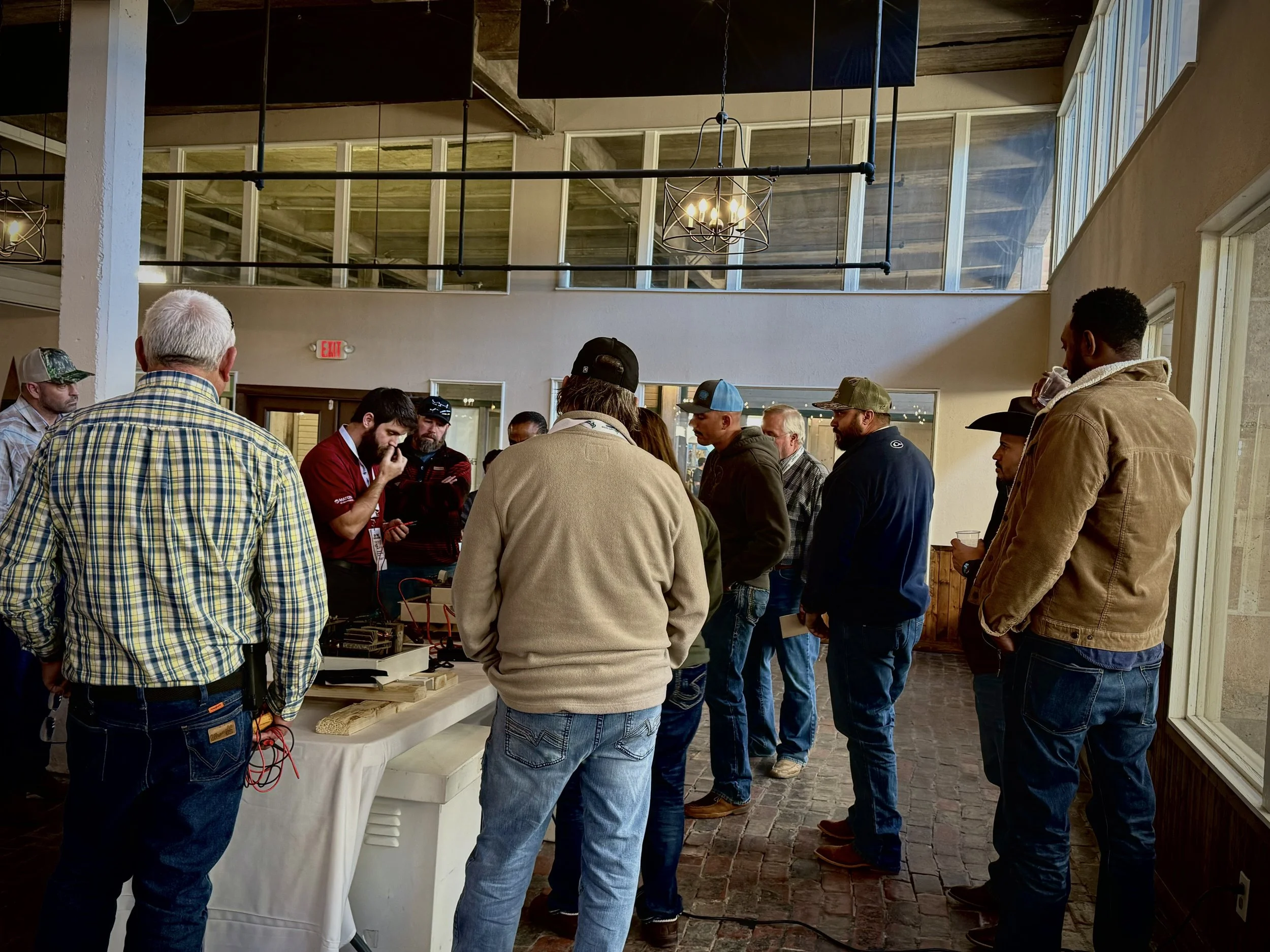 People standing in line inside a rustic building with wooden beams and large windows, waiting for an event or service.