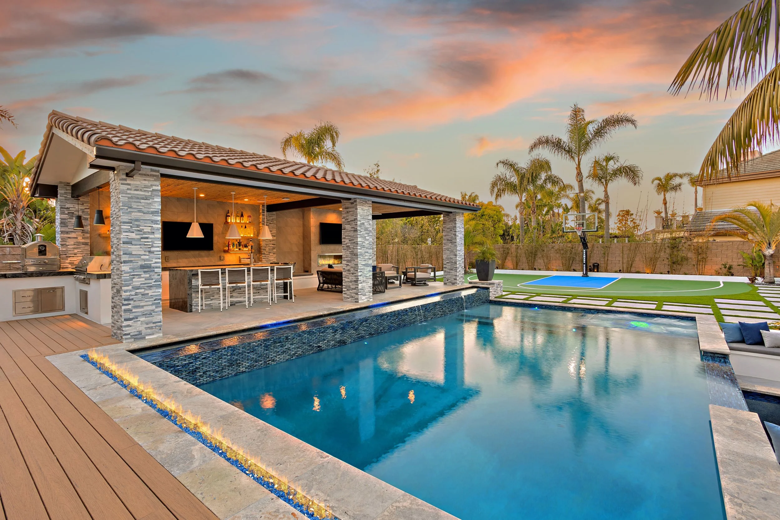 Luxury outdoor living area with a pool, modern kitchen, and basketball court in Huntington Beach, designed by VW Design and Build.