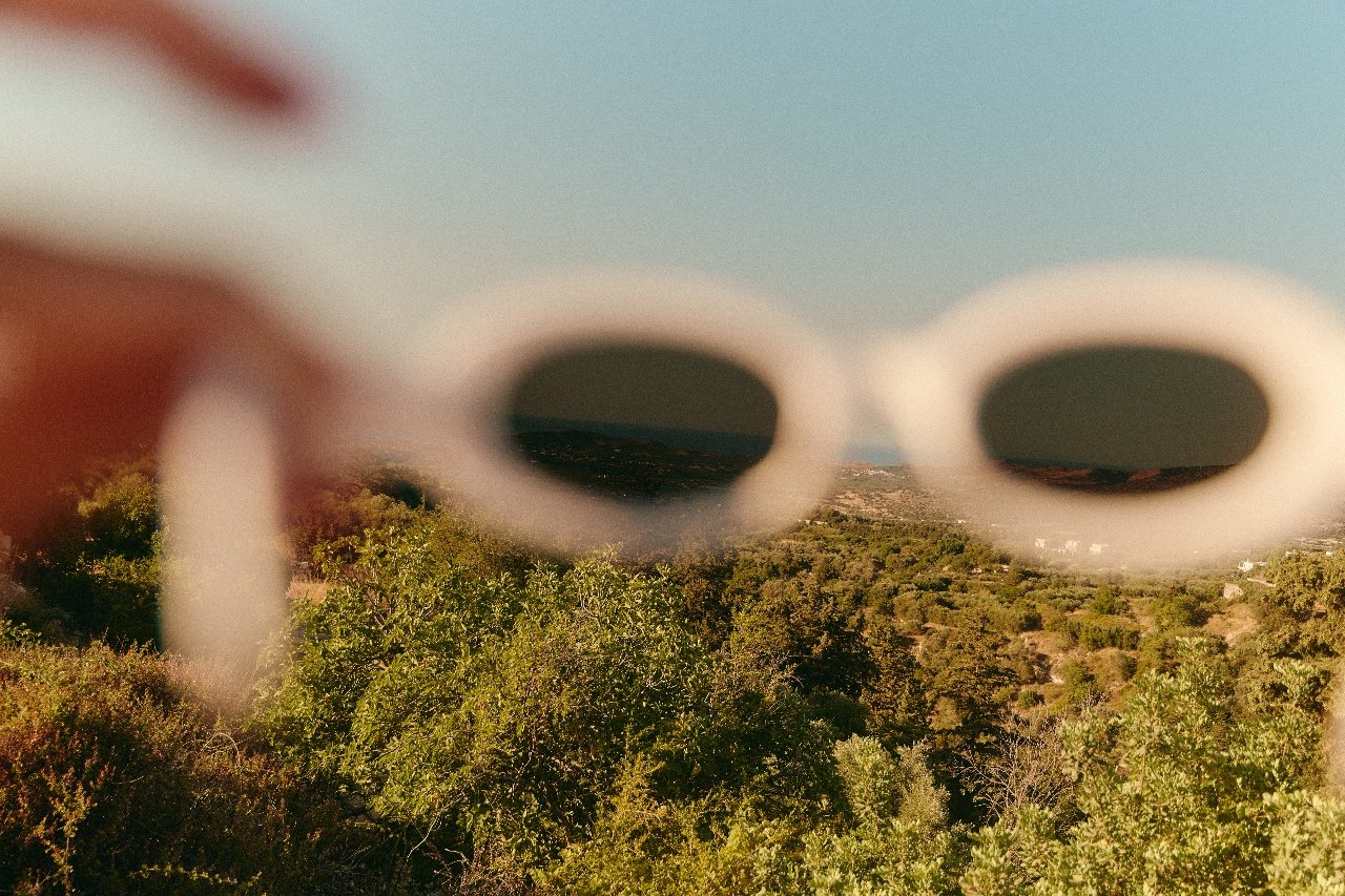 Blurred sunglasses held up against a sunlit landscape, symbolizing viewing your own path through your own lens