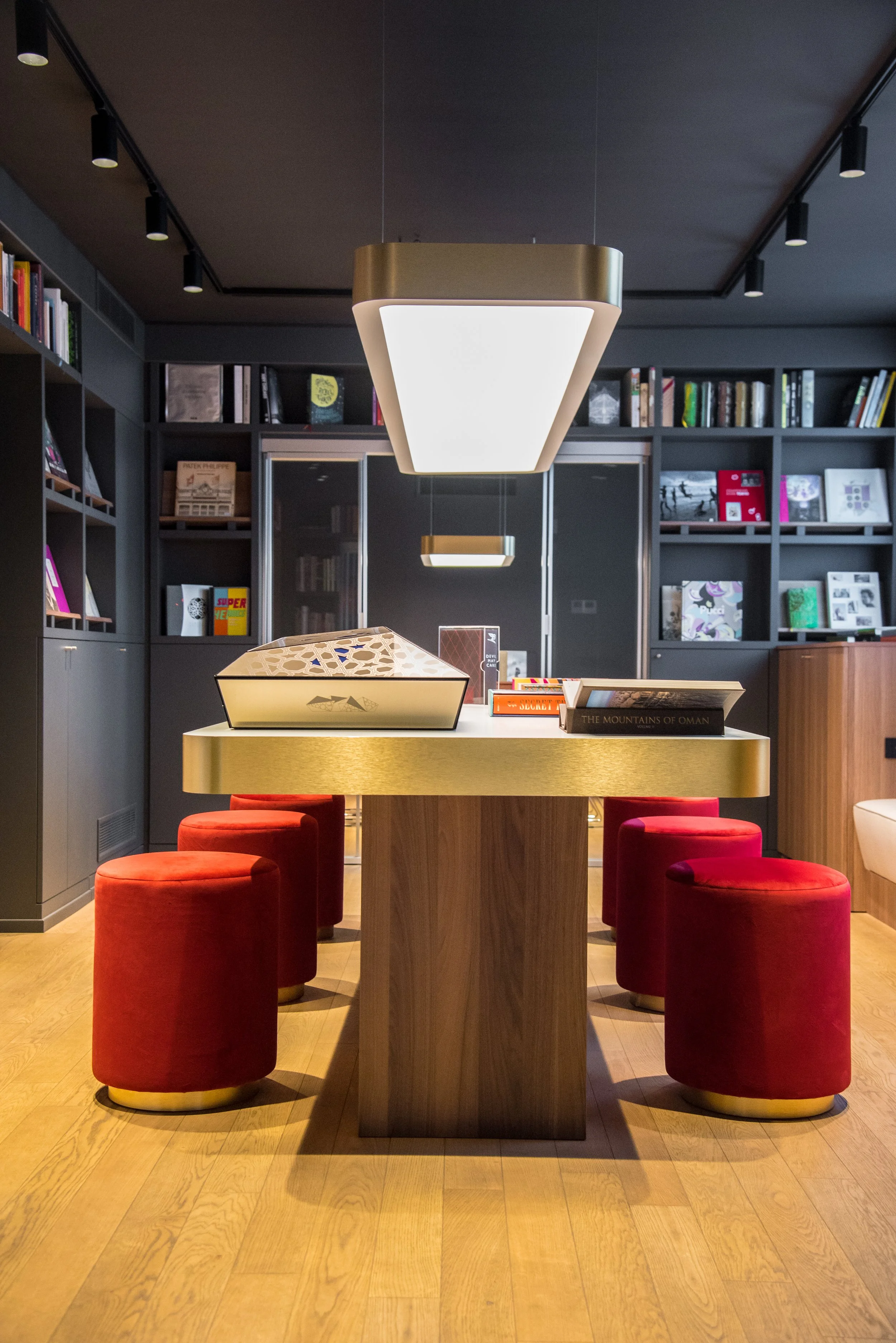 Sala con tavolo bianco, sei sgabelli rossi, librerie nere e lampade a soffitto.