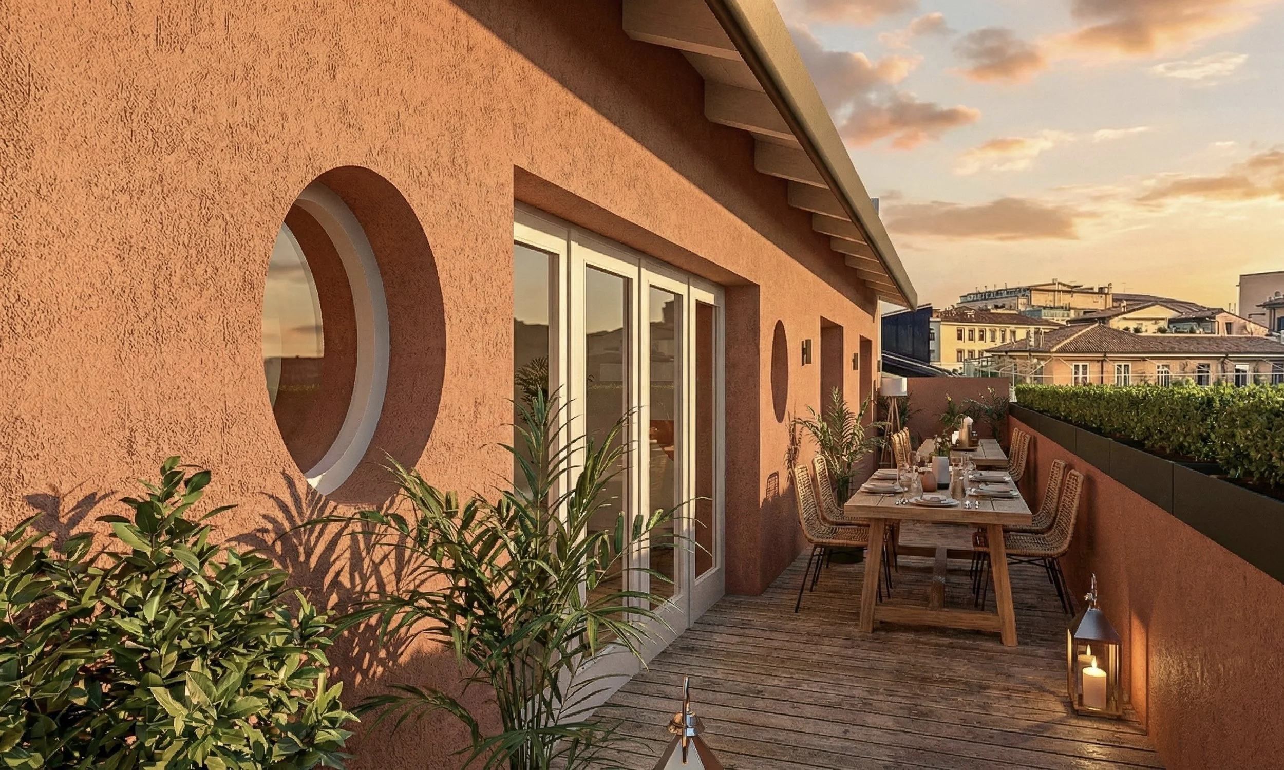 Balcone con tavolo apparecchiato, piante e lanterne durante il tramonto con un cielo arancione.