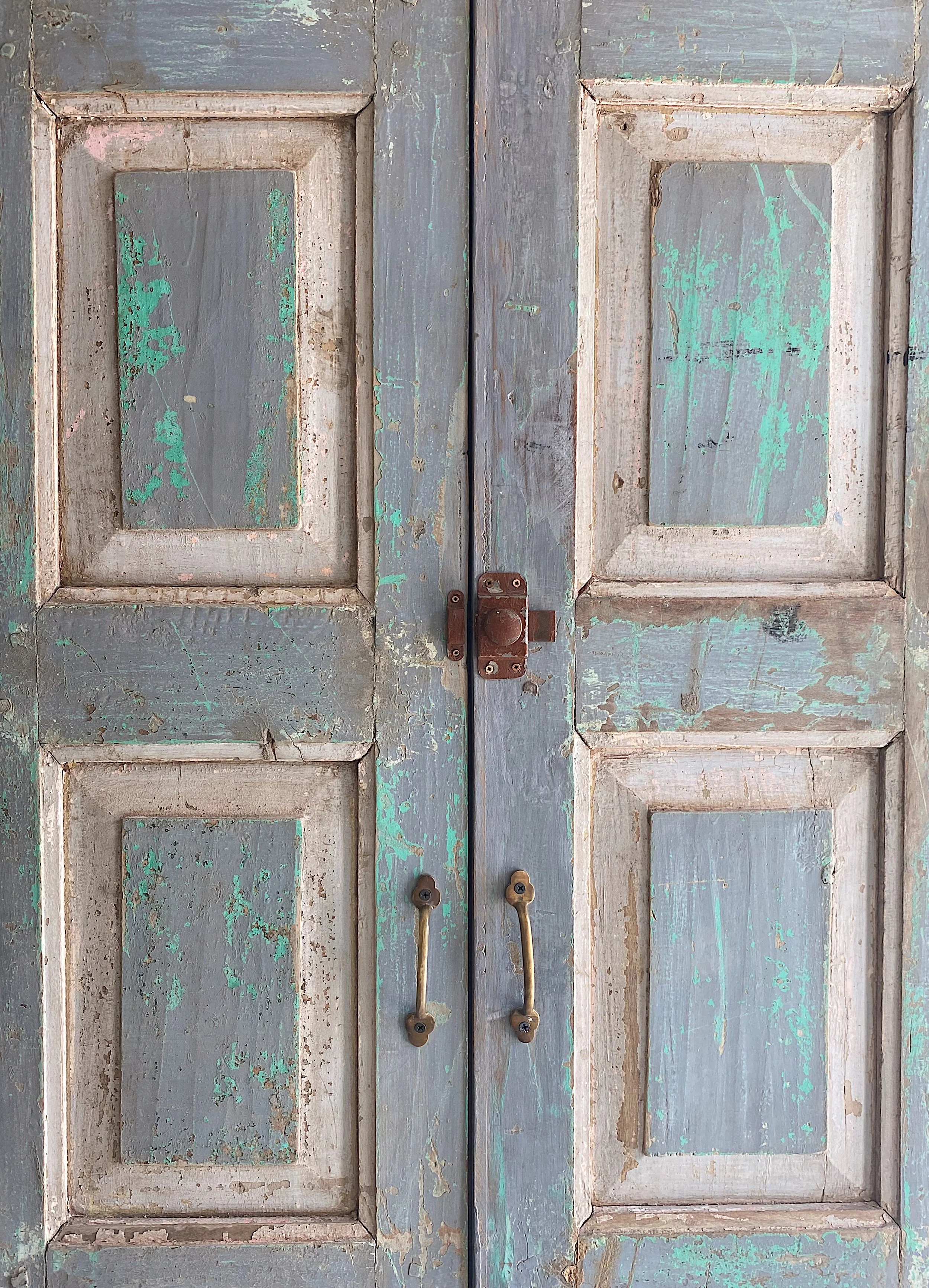 Antica porta in legno con scrostature e vernice verde, maniglie e chiusure di metallo.