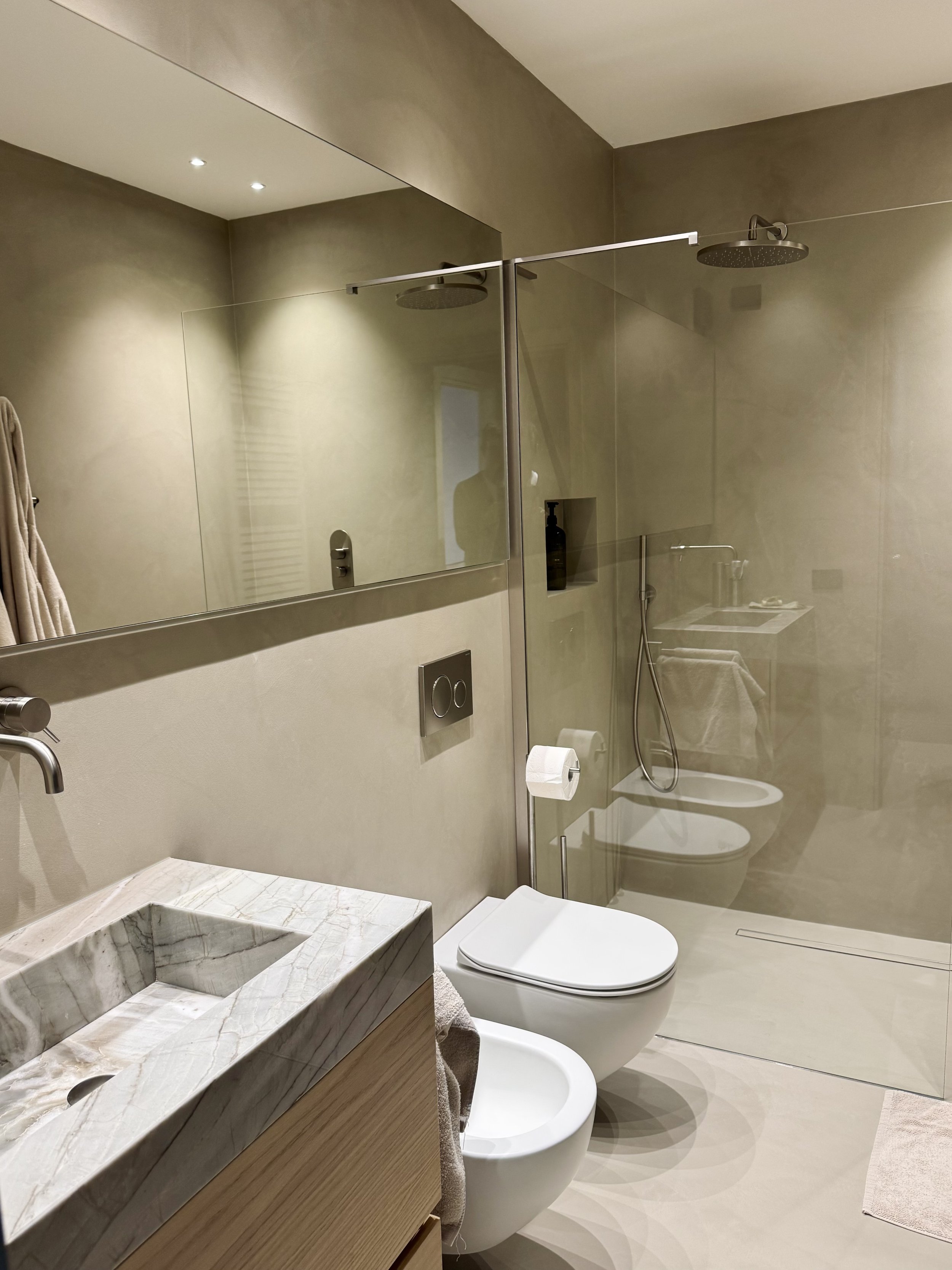 Bagno moderno con lavabo in marmo, specchio grande, WC e doccia con pareti di vetro