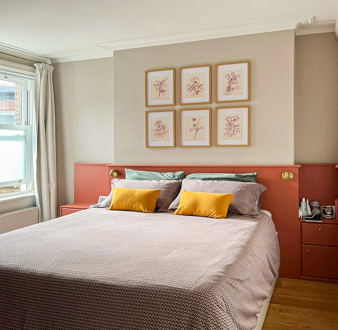 Camera da letto con letto matrimoniale, cuscini gialli e verdi, quadro con disegni di fiori sopra la testata, finestra a sinistra, arredamento in stile moderno e colori pastello.