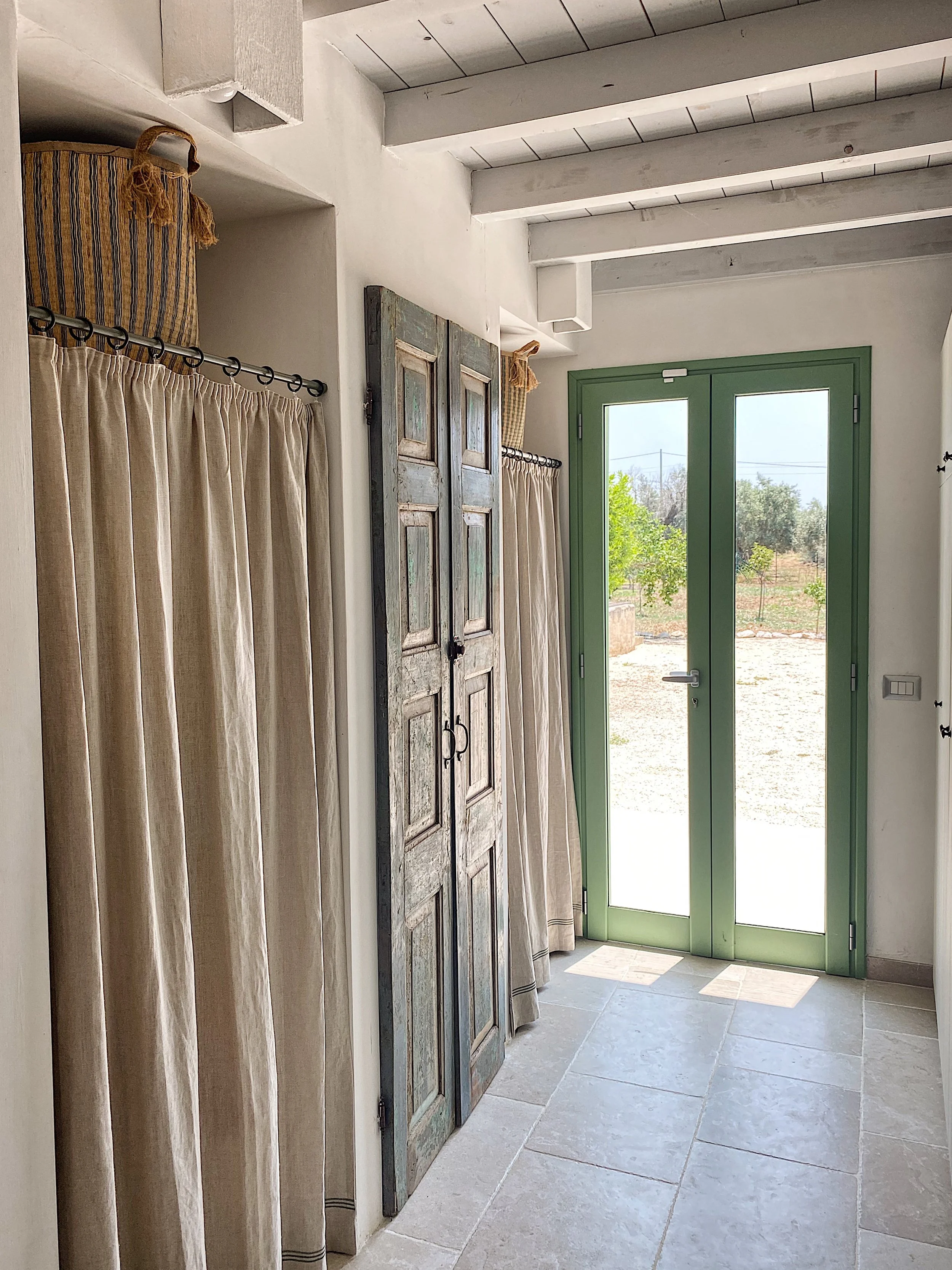 Entrata di una casa con porta in vetro verde, tende beige e una credenza di legno vecchio con due ante.