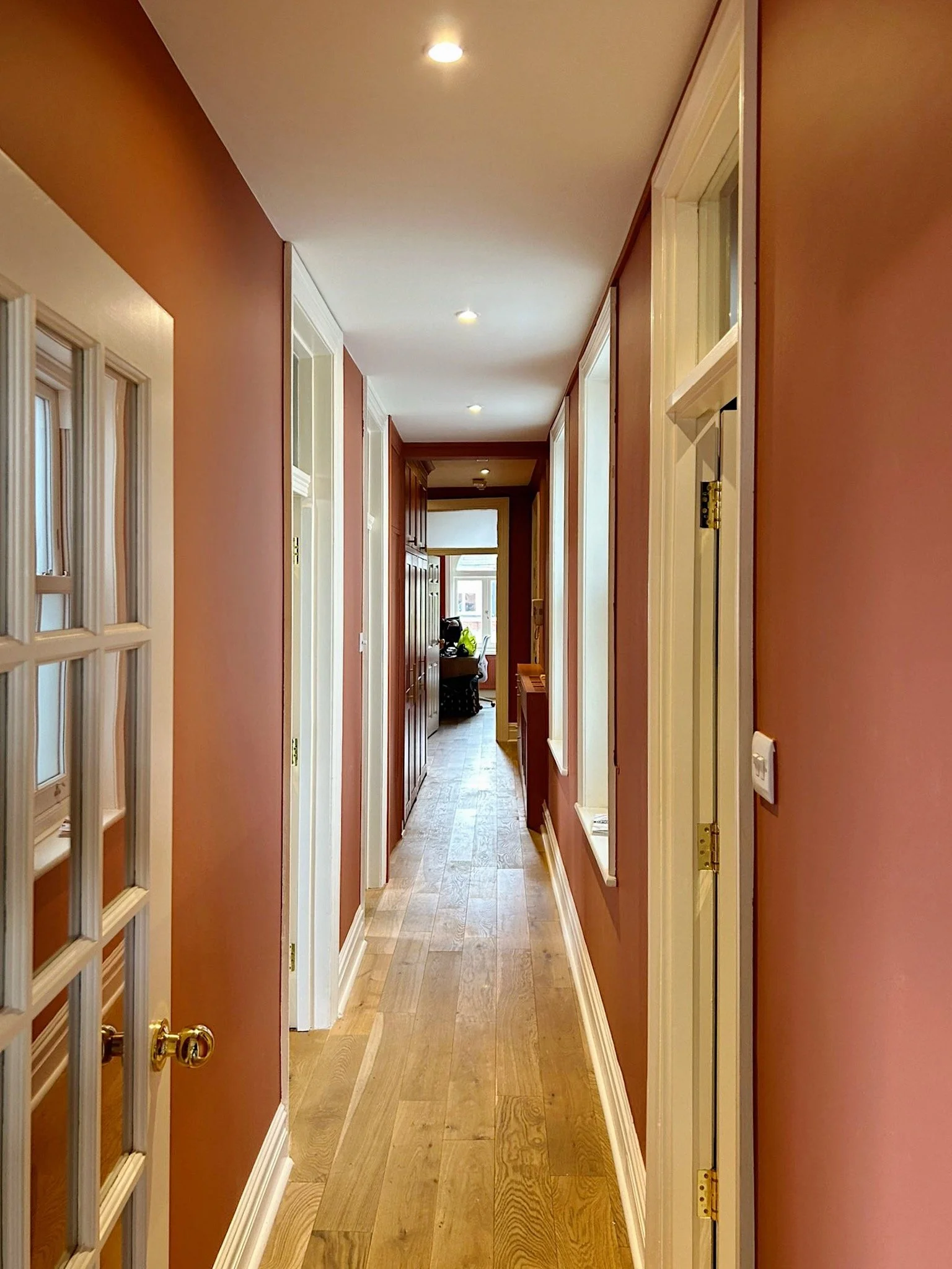 Corridor di una casa con pareti color terracotta, pavimento in legno chiaro, infissi bianchi e luce soffusa