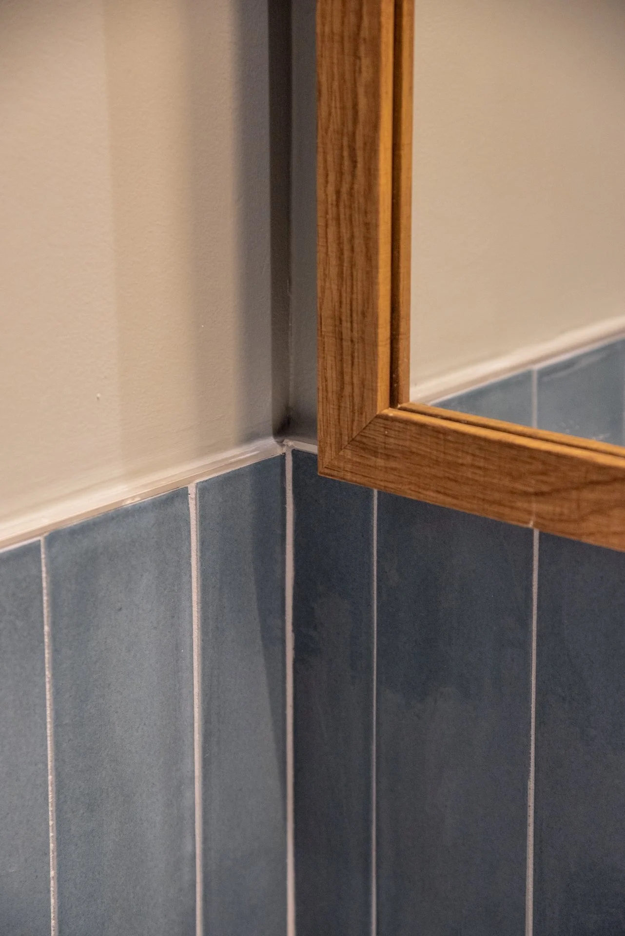 Dettaglio di un angolo di parete con rivestimento in piastrelle blu e uno specchio con cornice di legno.