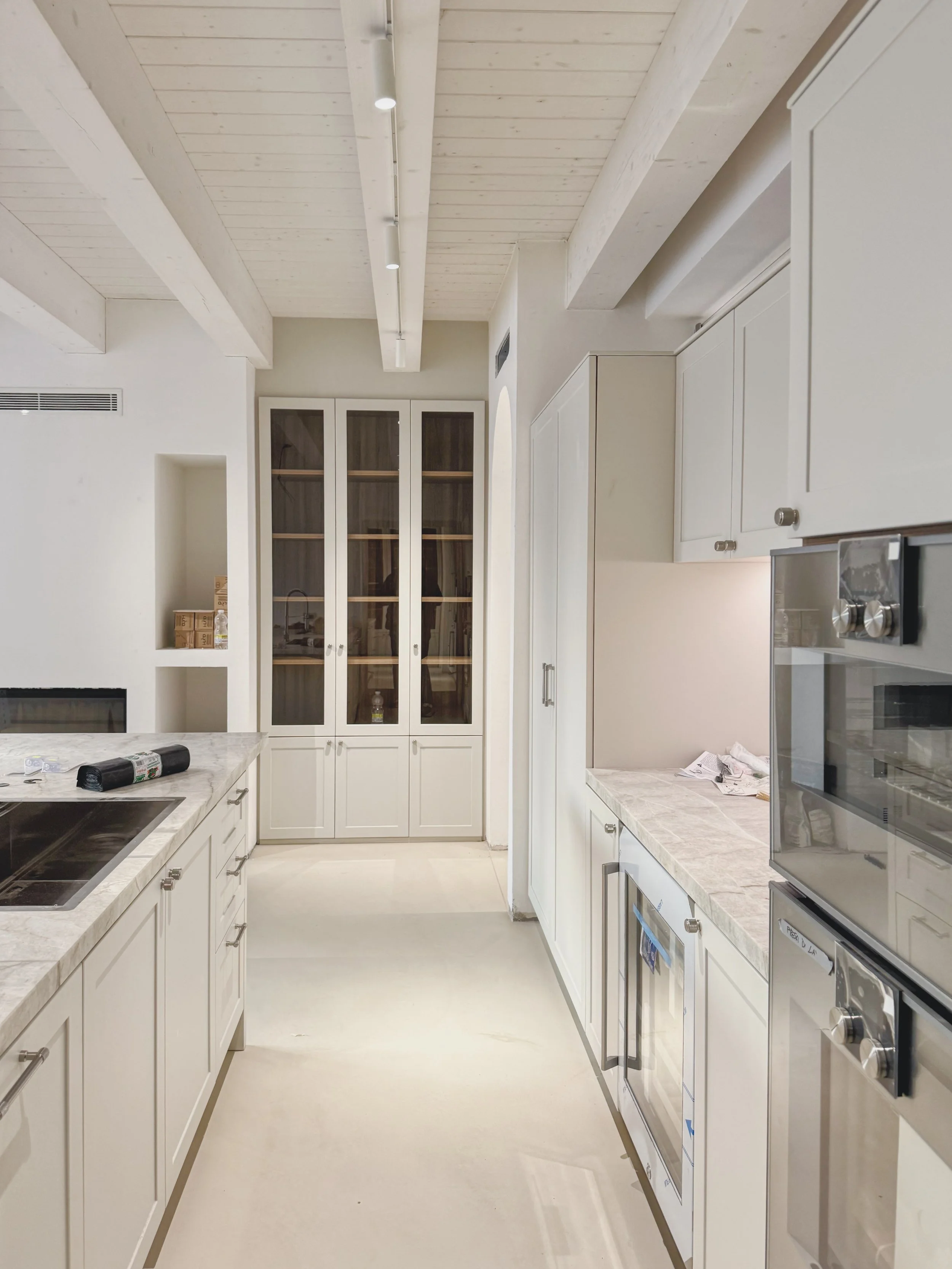 Cucina moderna con pensili bianchi, piani in marmo, forno e cucina a incasso, pareti e soffitto in legno chiaro, illuminazione a soffitto