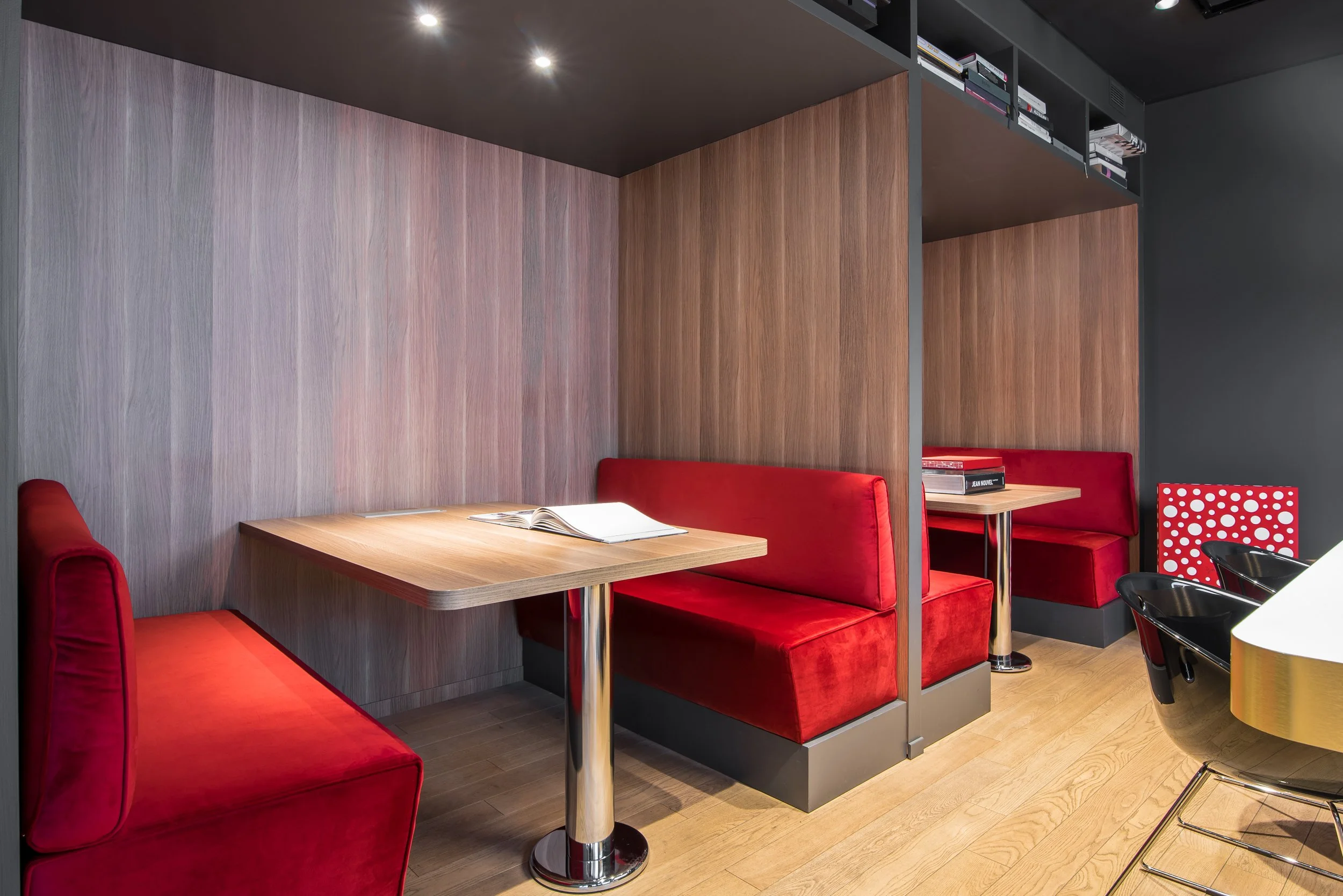 Ingressi con banconi con sedili rivestiti in velluto rosso e tavoli di legno, pareti in legno e nero, scaffali con libri e decorazioni, pavimento in legno.