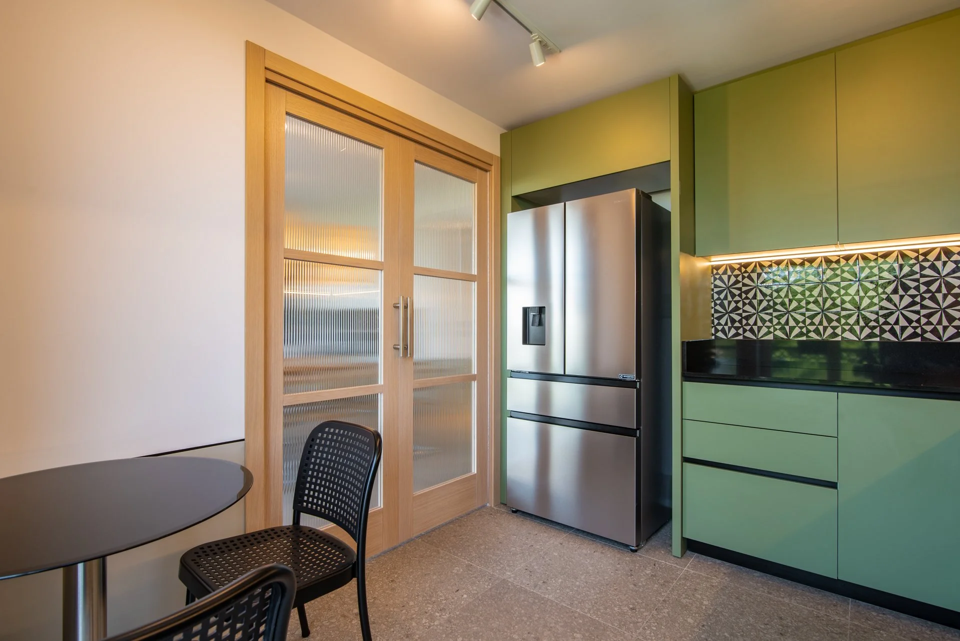 Cucina moderna con frigorifero in acciaio inox, armadietti verdi, piano di lavoro nero con piastrelle geometriche in bianco e nero