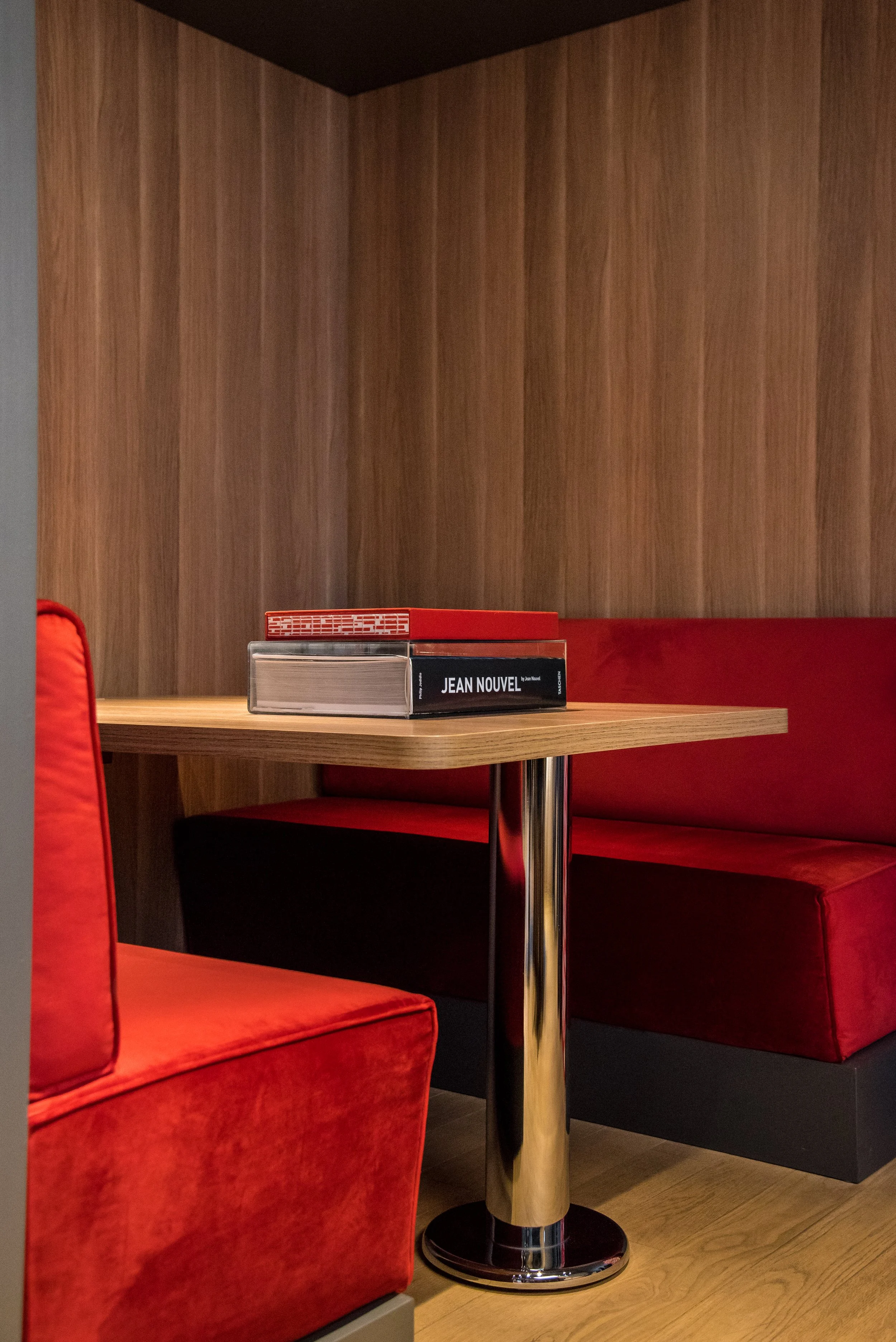 Angolo di un bar o ristorante con sedie e bancone in legno, libri posizionati sul tavolo, pareti di legno e arredamento moderno.