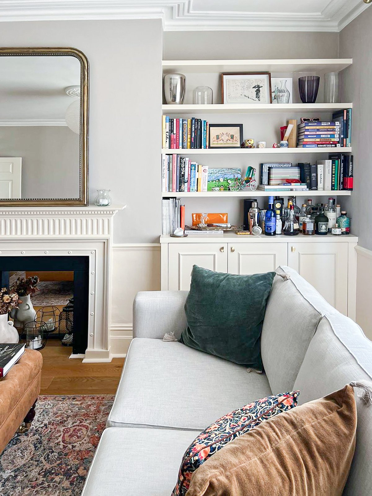 Interno di soggiorno con divano, libreria con libri e bottiglie, camino con decorazioni, grande specchio