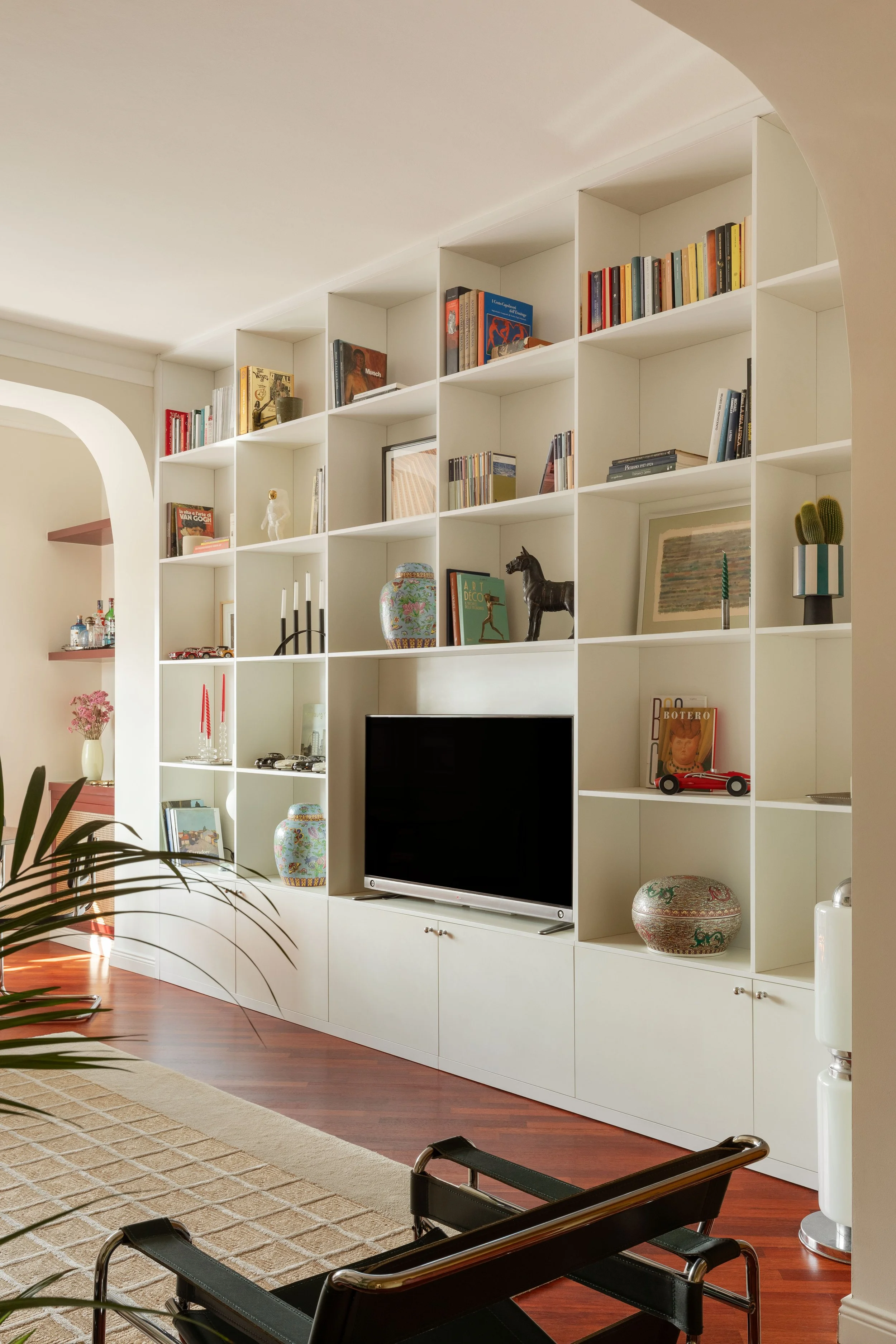 Sala con libreria bianca, tv, oggetti decorativi e piante, con pavimento in legno e un tappeto beige