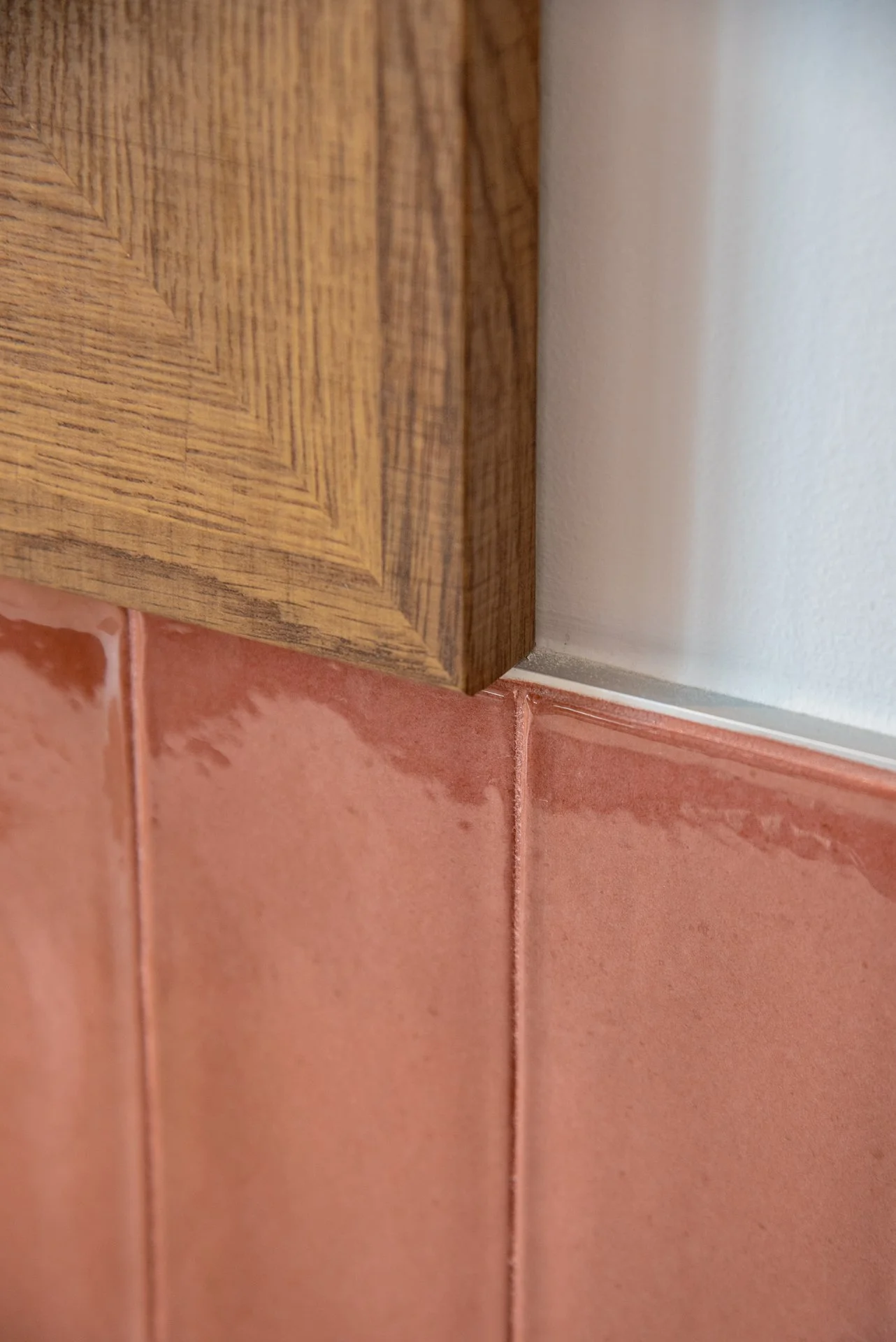 Dettaglio di angolo tra parete di cartongesso, rivestimento in legno e piastrelle rosa sulla parete inferiore.
