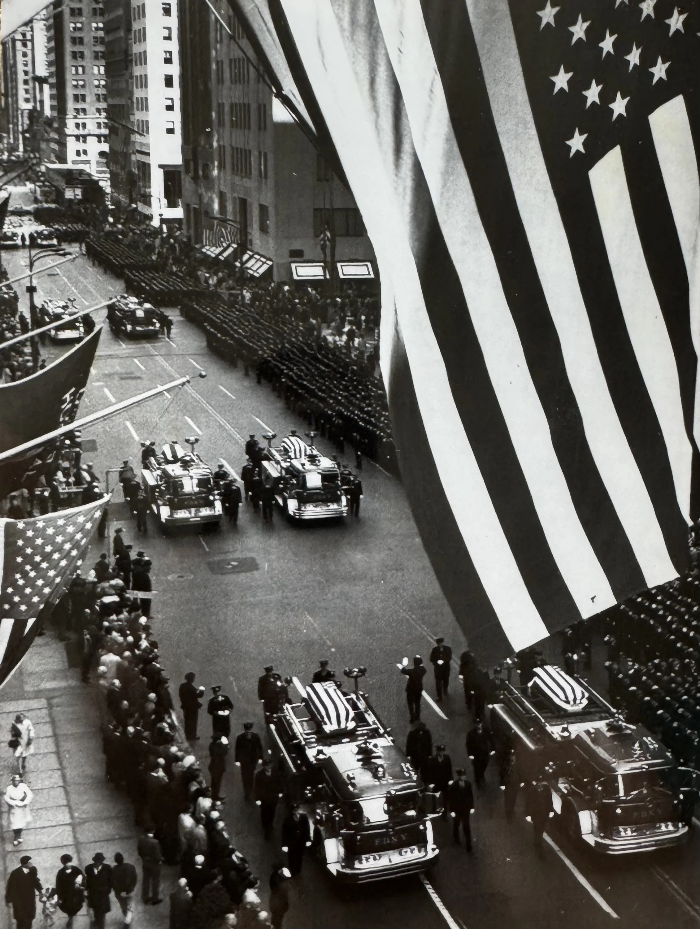 Veduta aerea della Fifth Avenue a New York nel 1966: camion dei pompieri con feretri e grande bandiera americana a mezz'asta in primo piano.