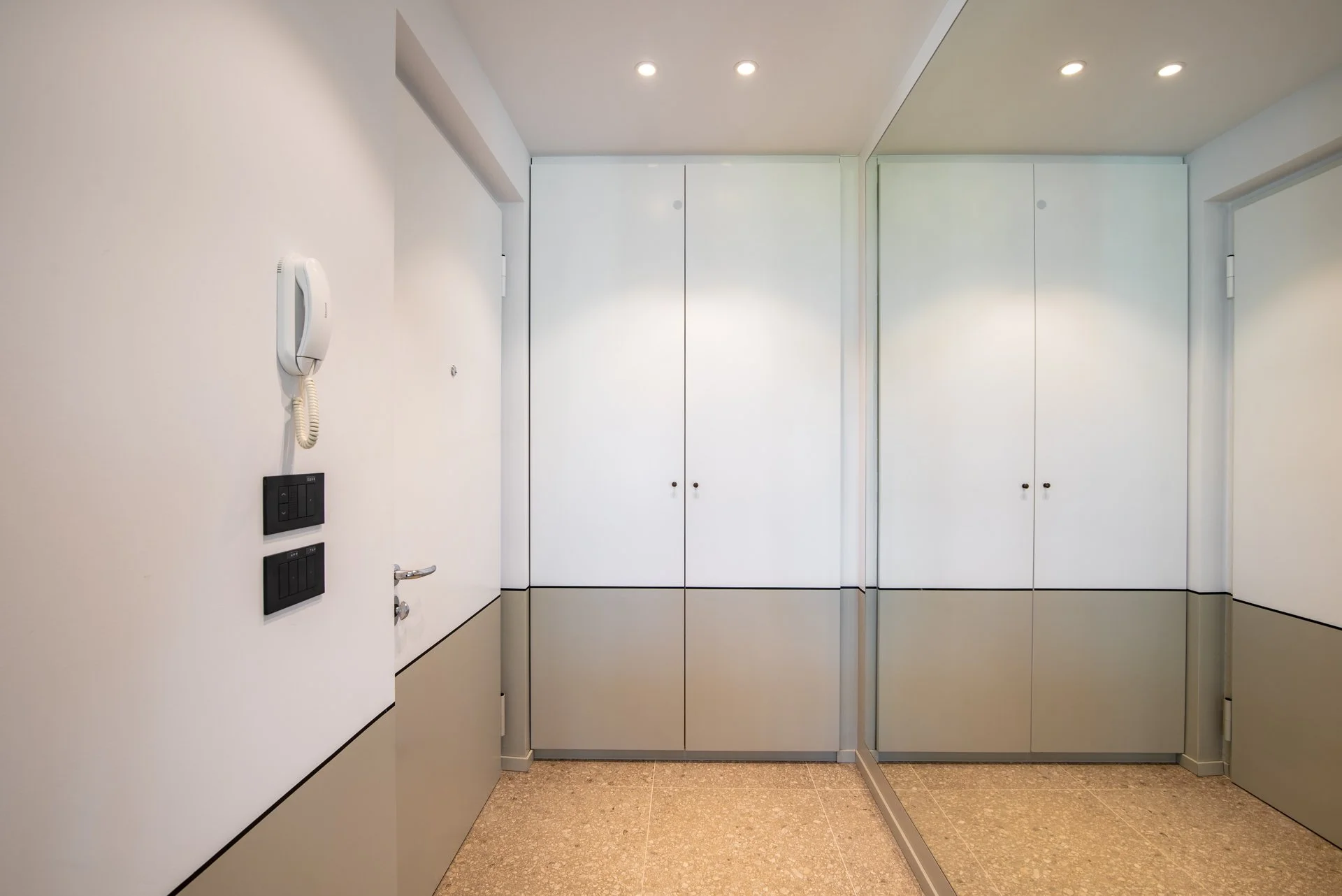 Ingresso di un appartamento con pareti bianche, armadi a muro bianchi, telefonino interfono e interruttori di luce.