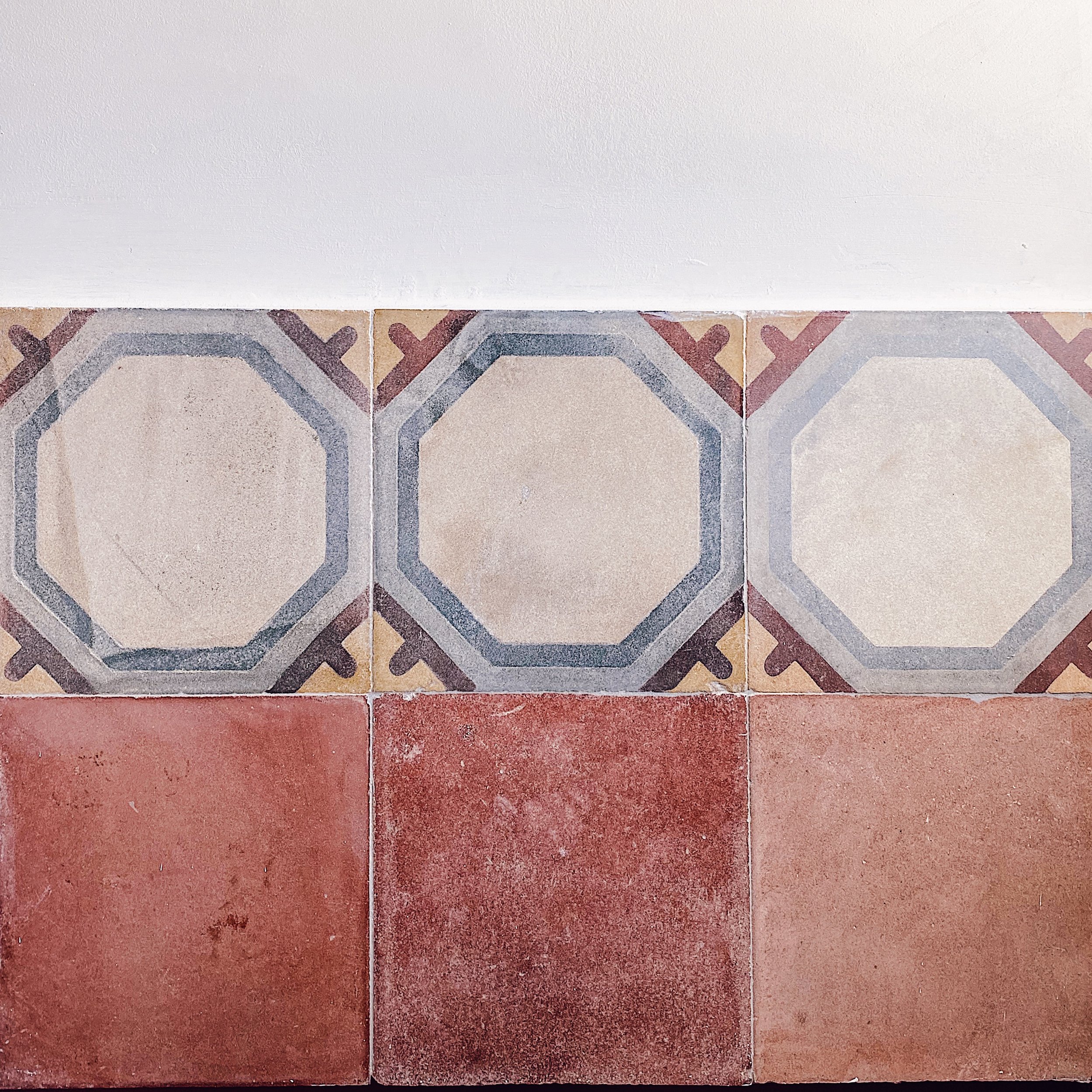 Tappeto di piastrelle con motivo geometrico, sopra un pavimento di piastrelle rosse.