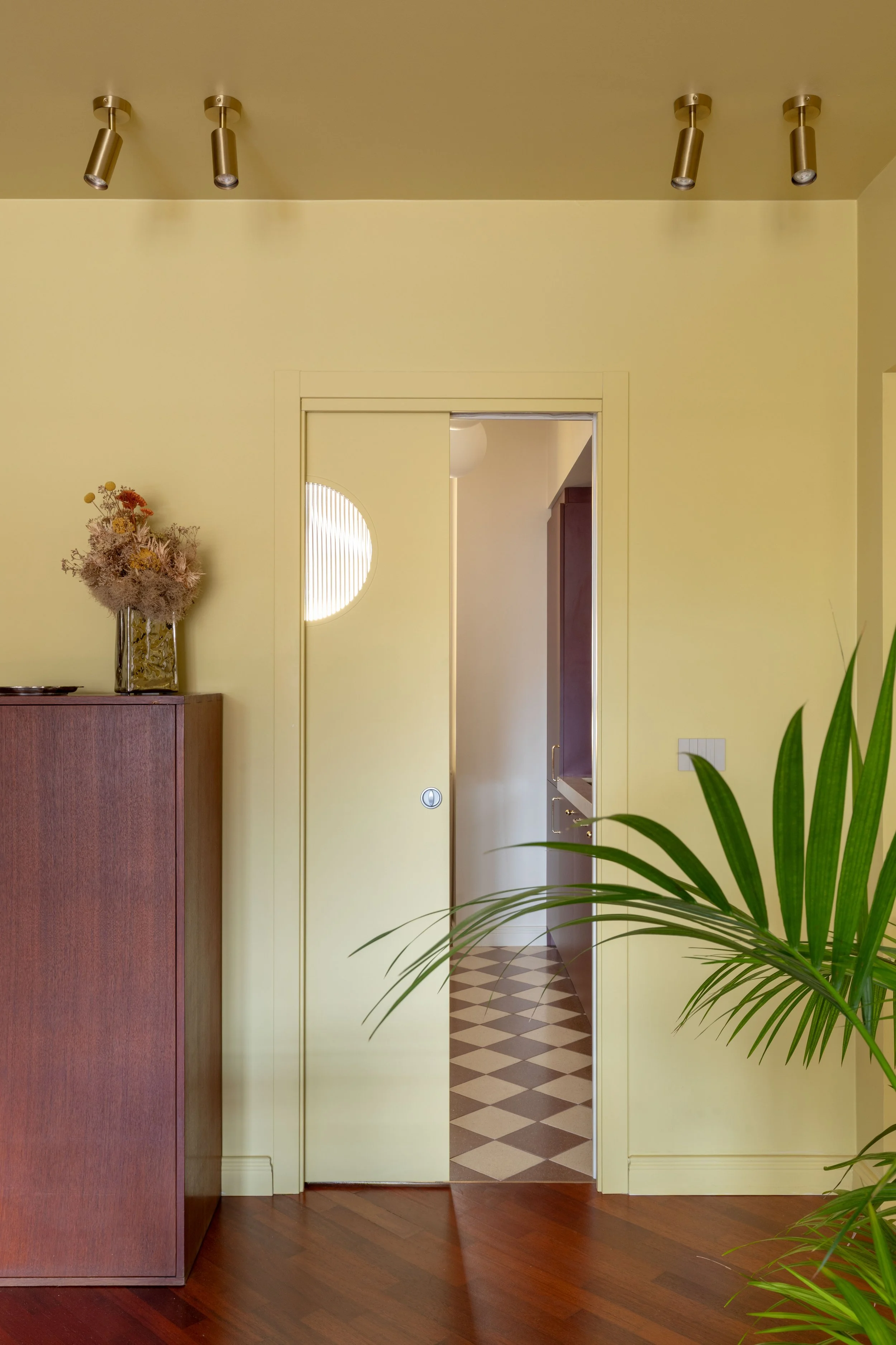 Ingresso di una casa con porta scorrevole aperta, pareti gialle, pavimento in parquet e un mobile con un vaso di fiori secchi
