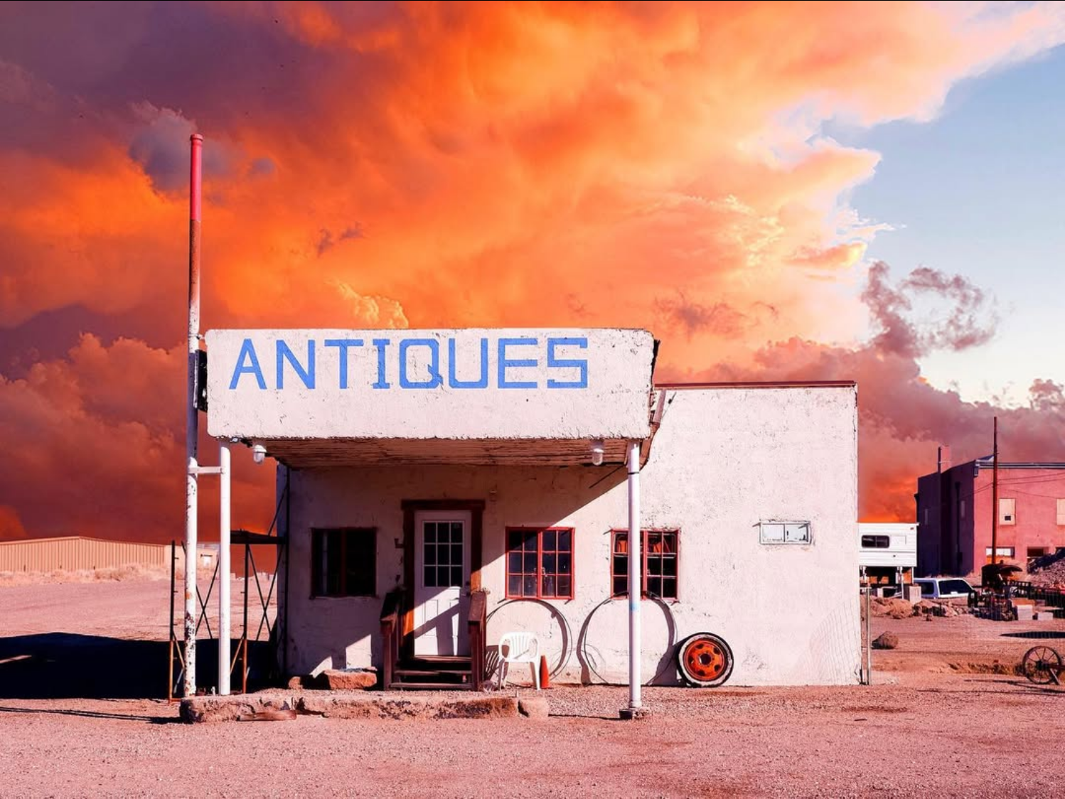 Fotografia di Chiara Bolognesi con l'insegna Antiques su un edificio bianco sotto un cielo arancione infuocato a Goldfield, ghost town nel Nevada.