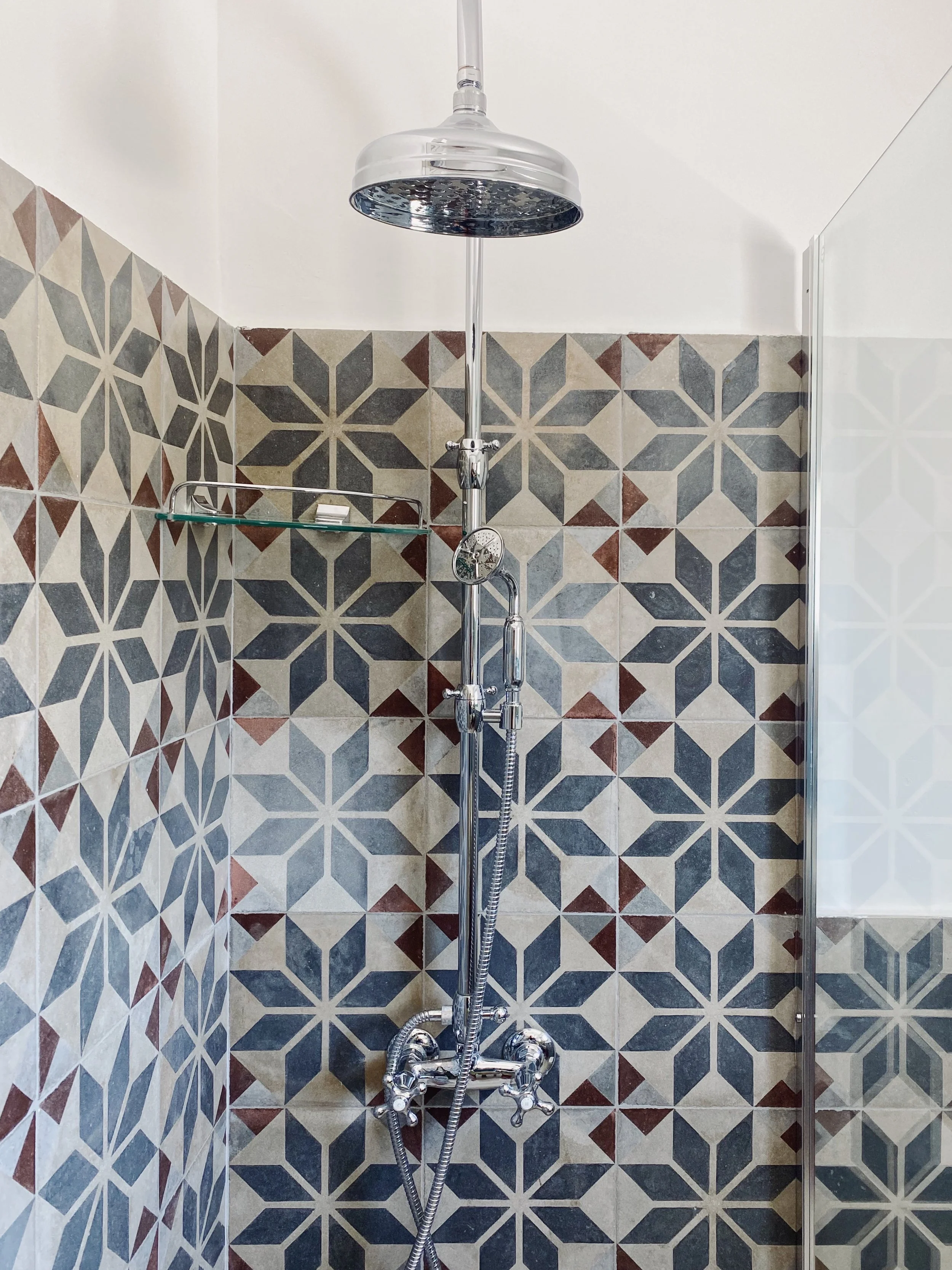 Doccia a pioggia con pareti di piastrelle decorative geometriche in tonalità di beige, grigio e rosso