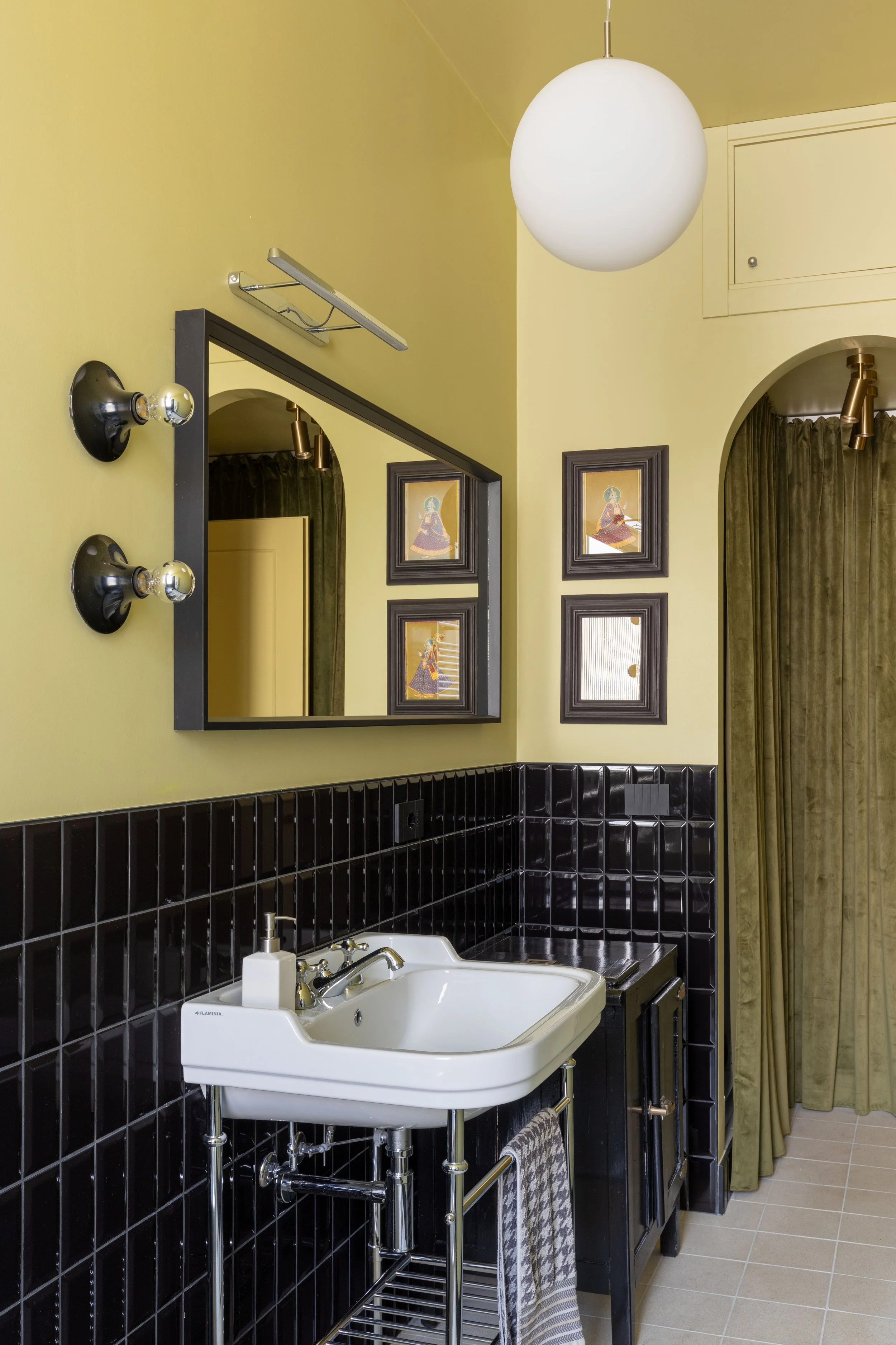Specchio, lampada wall-mounted, quadri alle pareti, lavandino con shampoo e asciugamano, tenda verde, lampada rotonda bianca