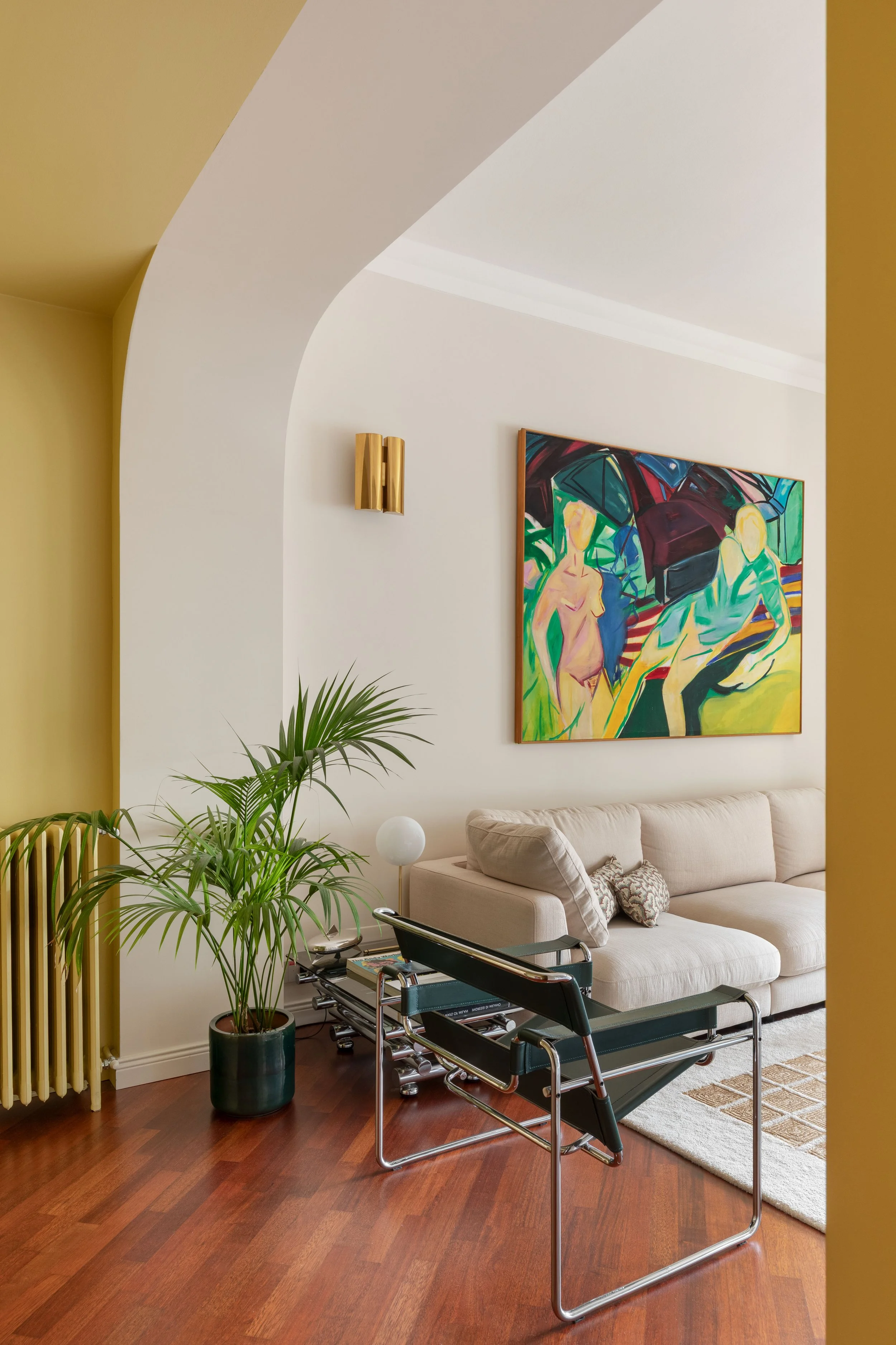 Soggiorno con divano beige, dipinto astratto alle pareti, pianta verde, lampada da terra bianca, sedia con rivestimento in tessuto blu, tappeto beige con motivo geometrico, pareti yellow e bianca, decorazioni moderne.