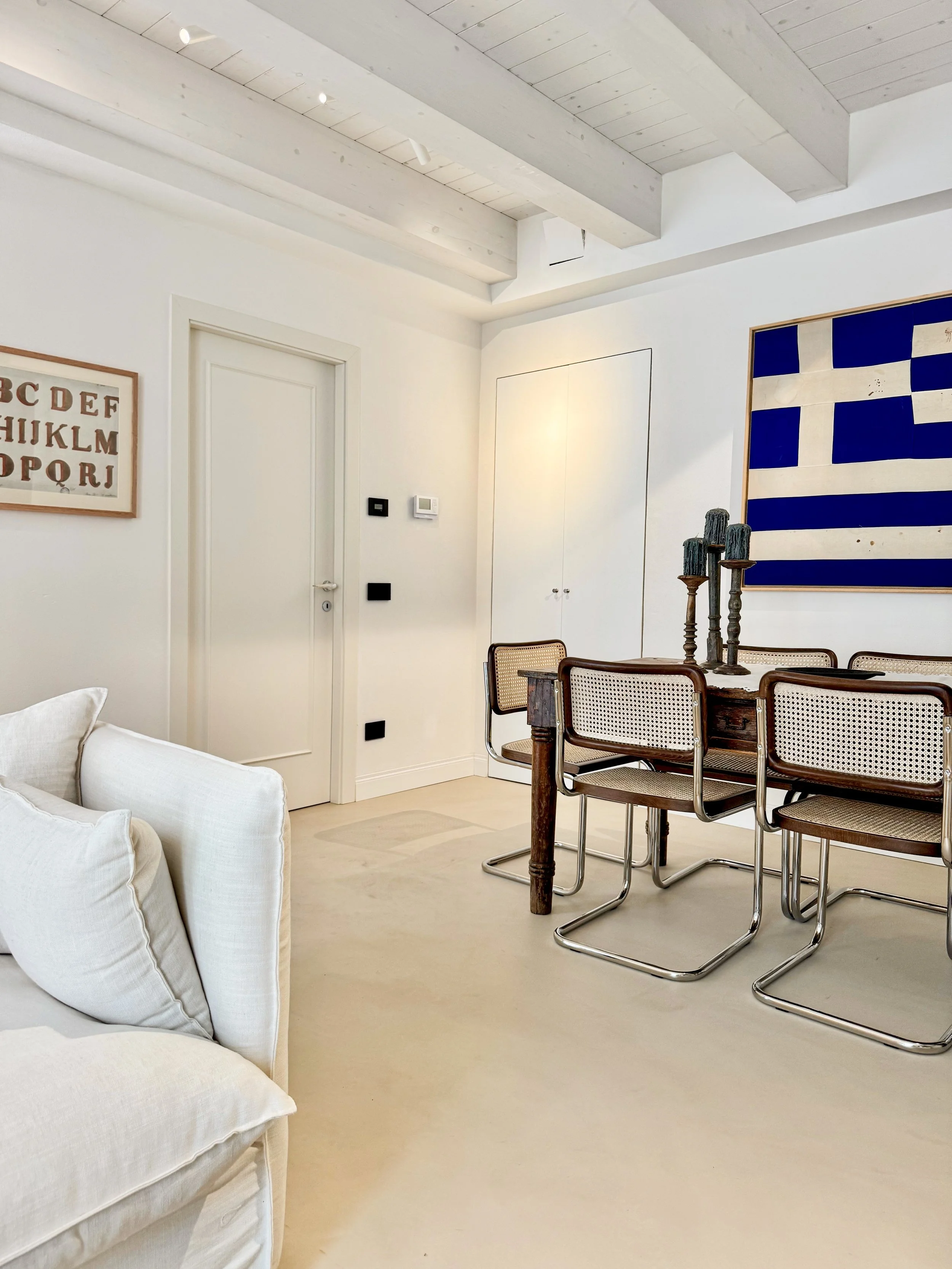 Interno di una stanza con pareti bianche, decorata con quadri, tavolo, sedie e divano.