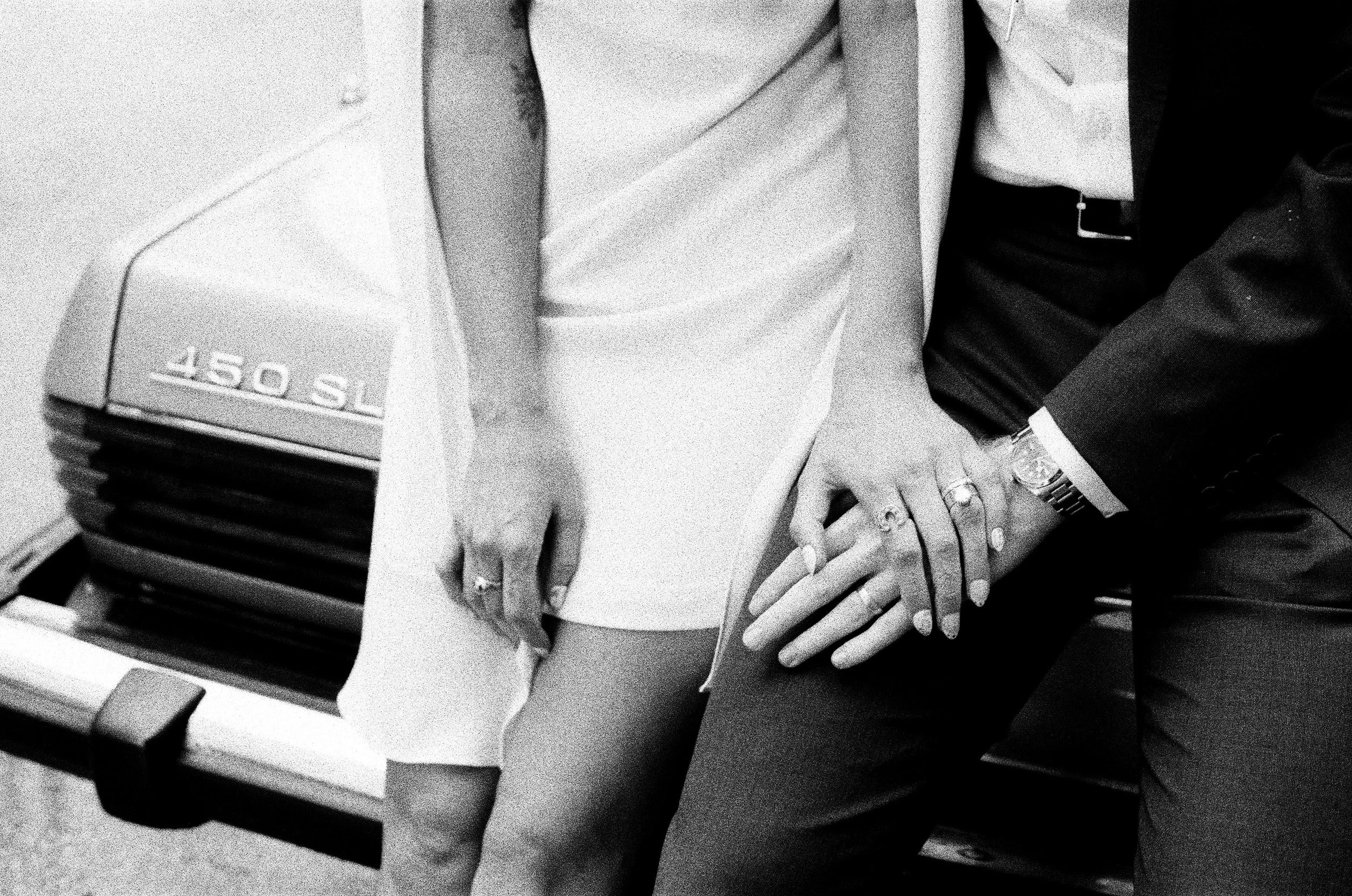 Newly weds show off their rings while sitting on the trunk of their vintage car
