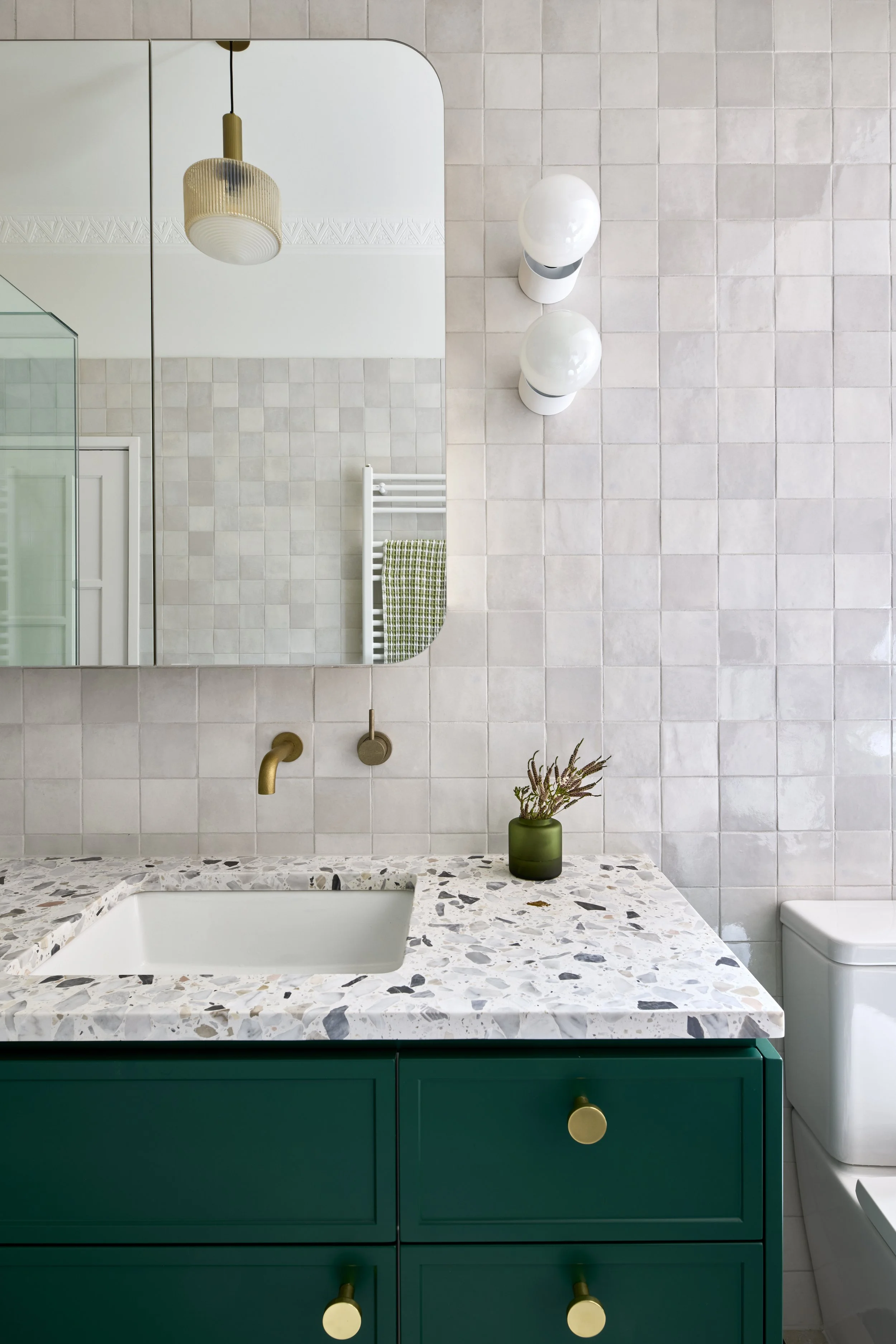 Modern bathroom vanity with green cabinets, terrazzo bench top and brass taps.