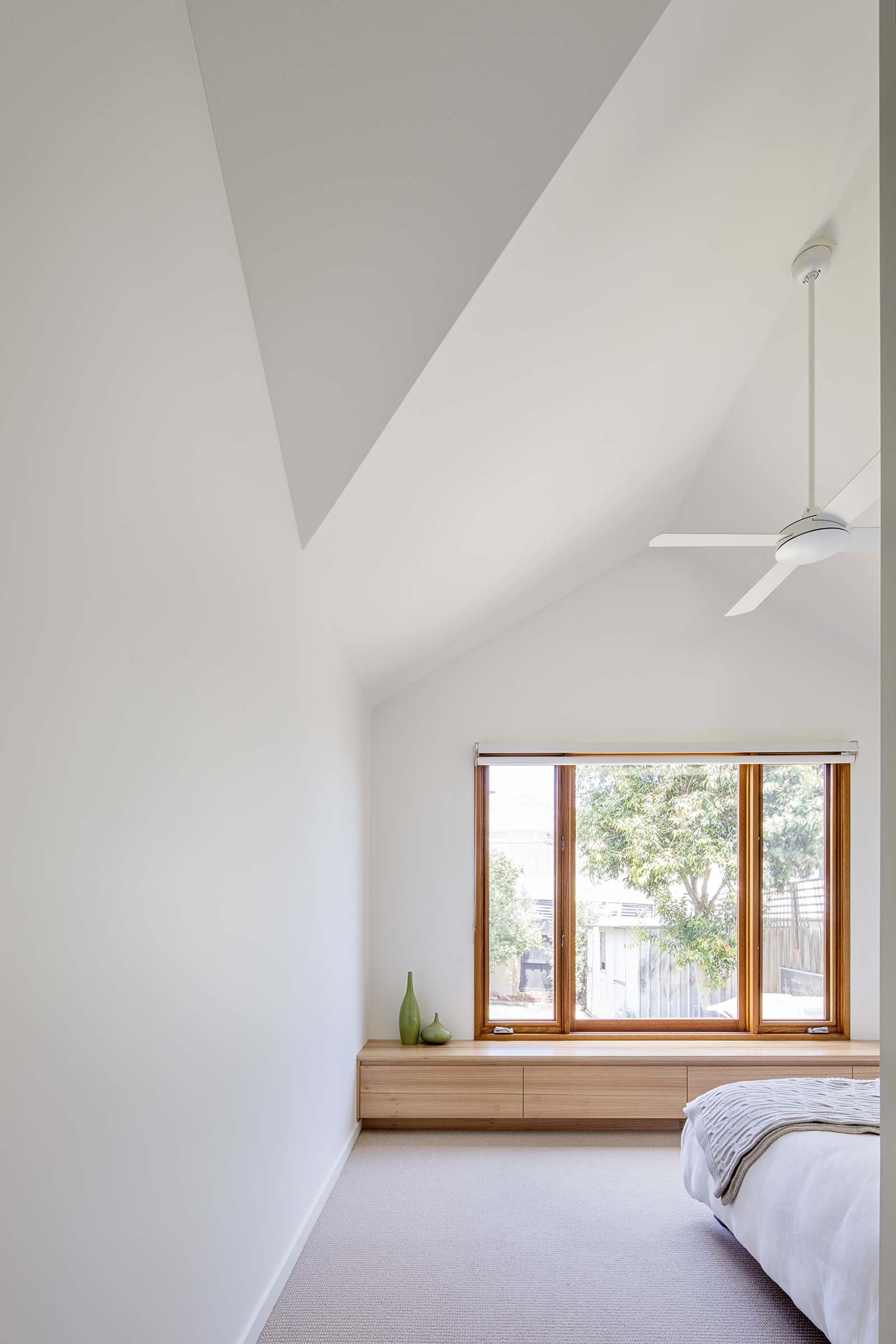 Modern bedroom with cathedral ceiling, fan and timber window seat.