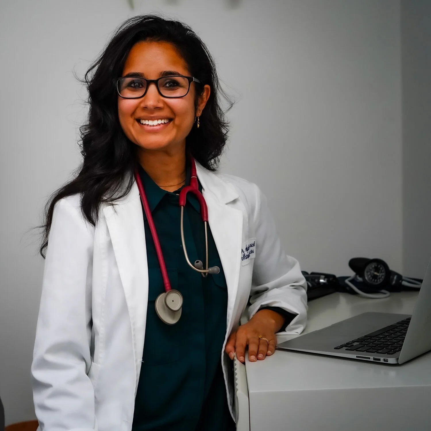 Female doctor wearing a white coat and stethoscope, standing by a laptop.