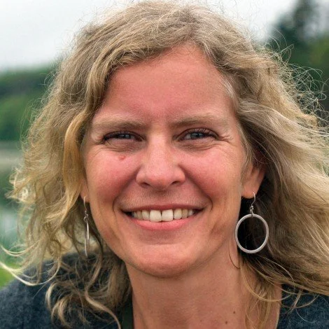 Woman smiling outdoors with curly hair and hoop earrings
