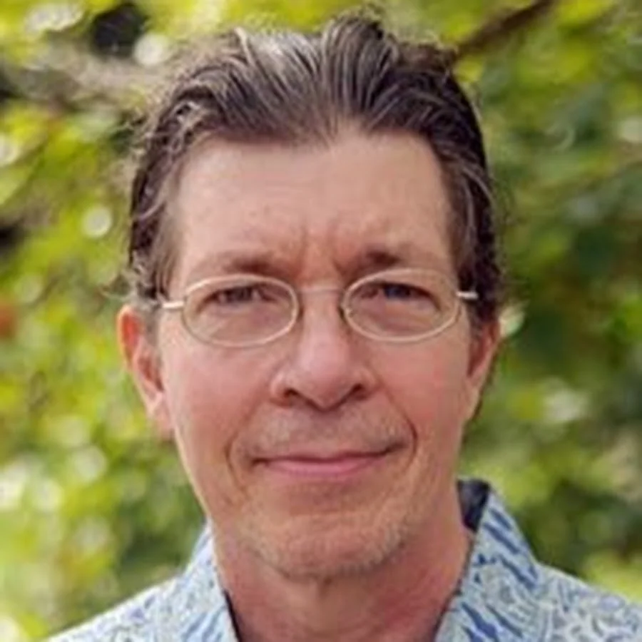 Man wearing glasses outdoors with a blurred green background.