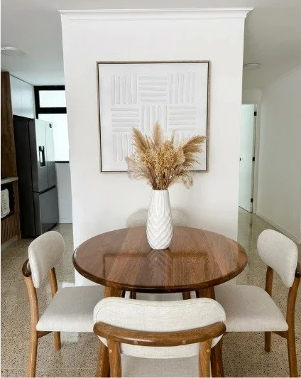 Villa Draga dining table detail — white ceramic vase with dried botanicals, textural wall art, warm wood table. Interior design by Melrose Home and Co.
