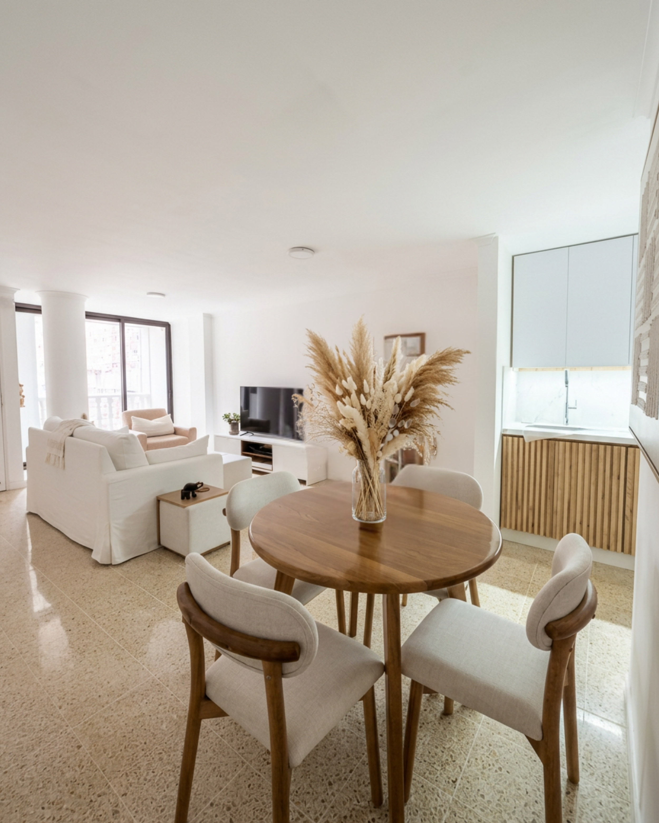 Villa Draga dining area with round walnut table, upholstered chairs, and dried pampas. Open plan view into living room. Interior design by Melrose Home and Co., Medellín Colombia.