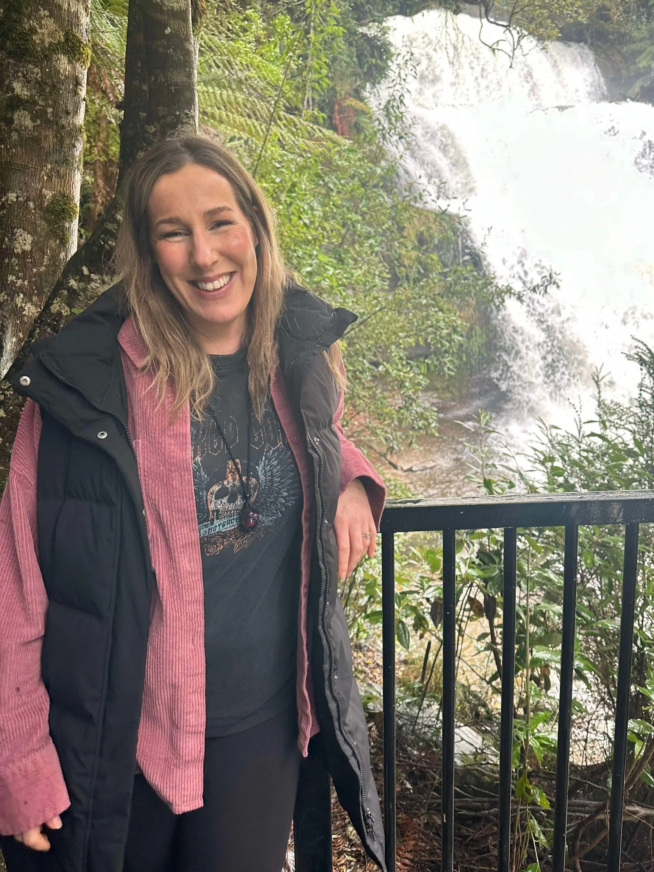 Woman smiling in front of a waterfall and greenery