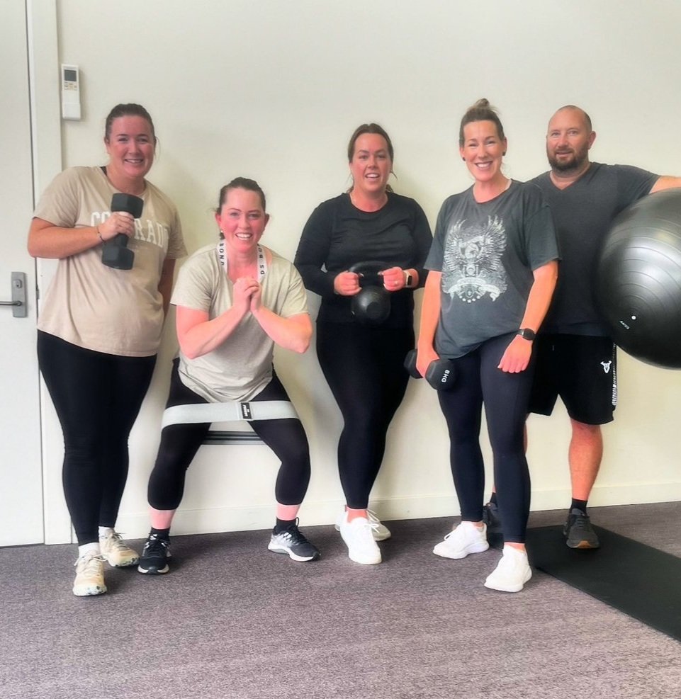 Group of five people in athletic clothing holding exercise equipment in a fitness studio.
