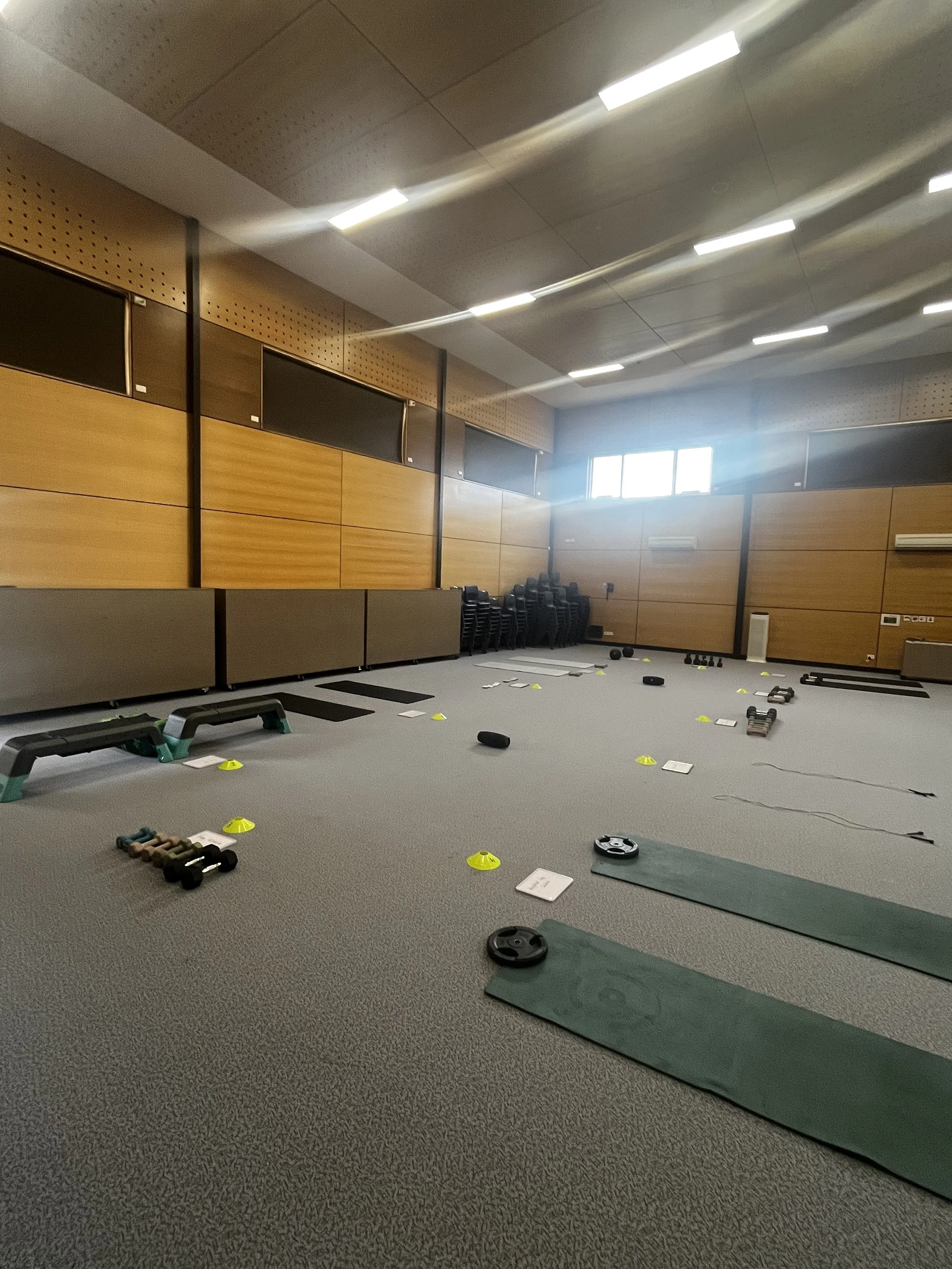 Indoor gym setup with exercise mats, dumbbells, cones, and fitness step platforms.