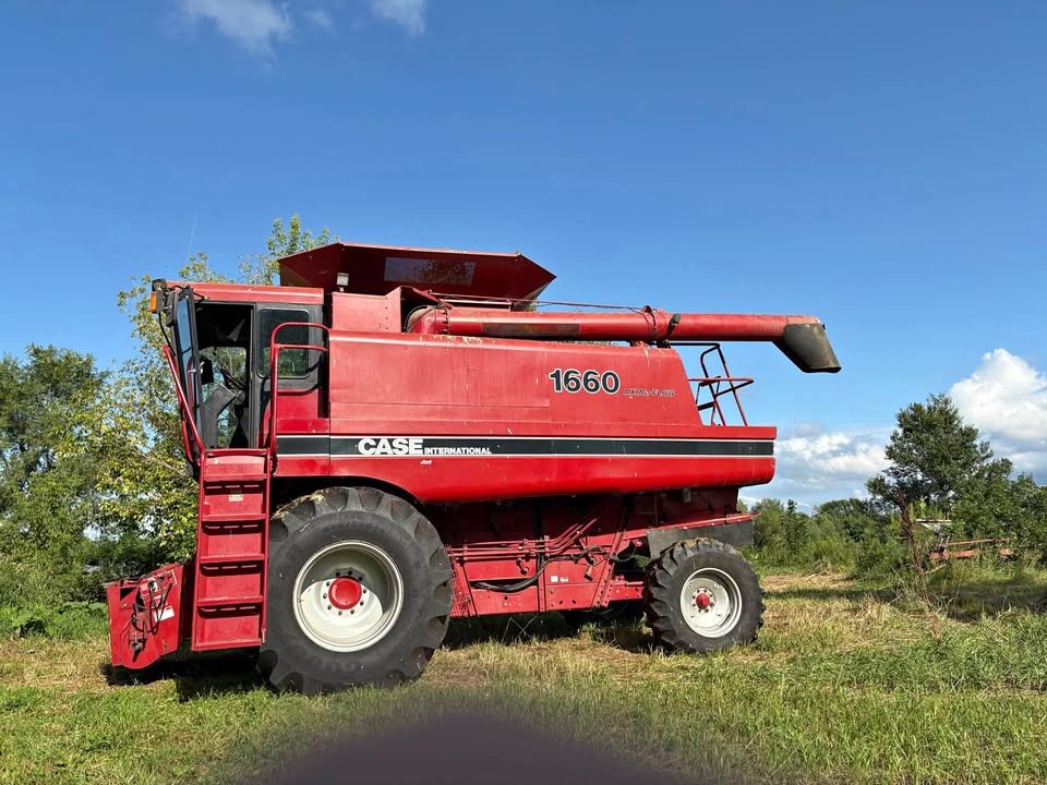 Red CASE INTERNATIONAL combine harvester in a grassy field under a blue sky with a few clouds.