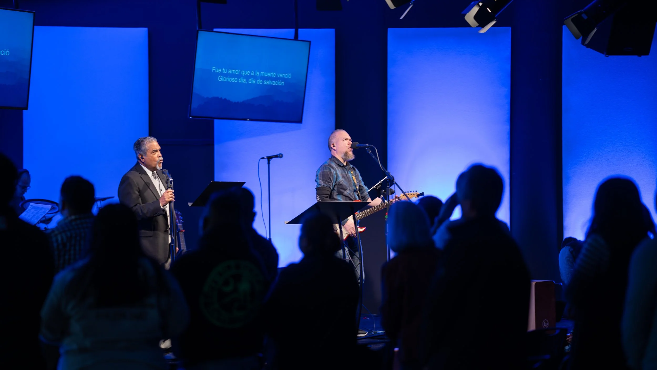 A church service or concert where a man is singing into a microphone and playing an electric guitar on stage, with an audience watching.