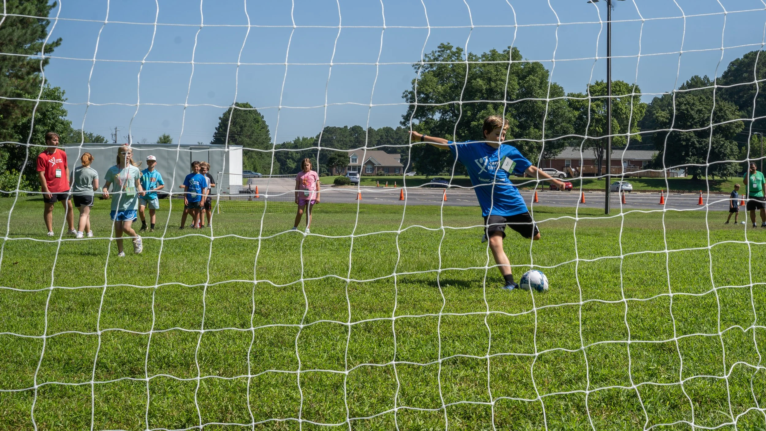 Kids playing soccer on a grassy field during daytime, viewed through a goal net.