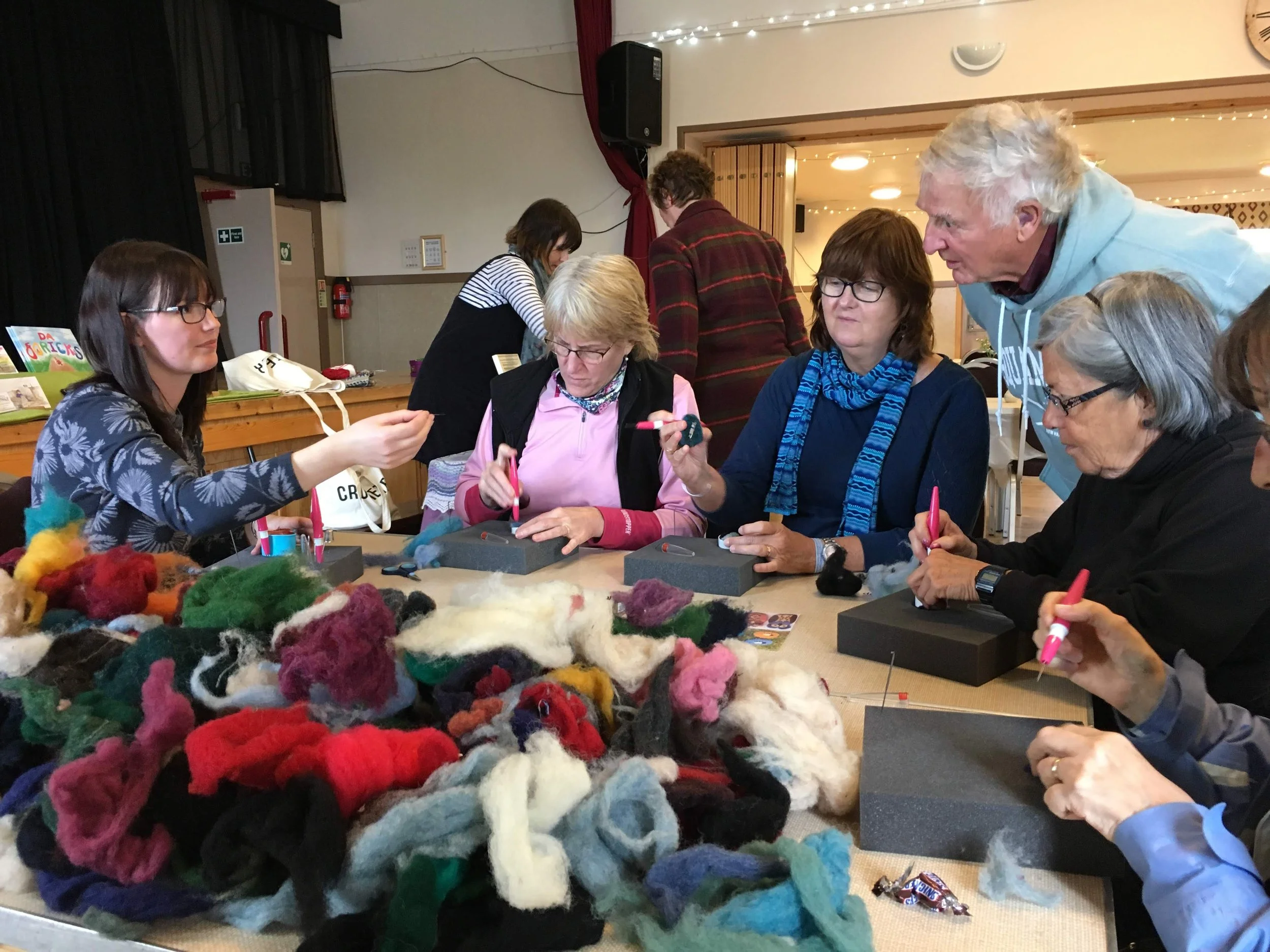 Group of people in a crafting session working with colorful wool and felting tools at a table.