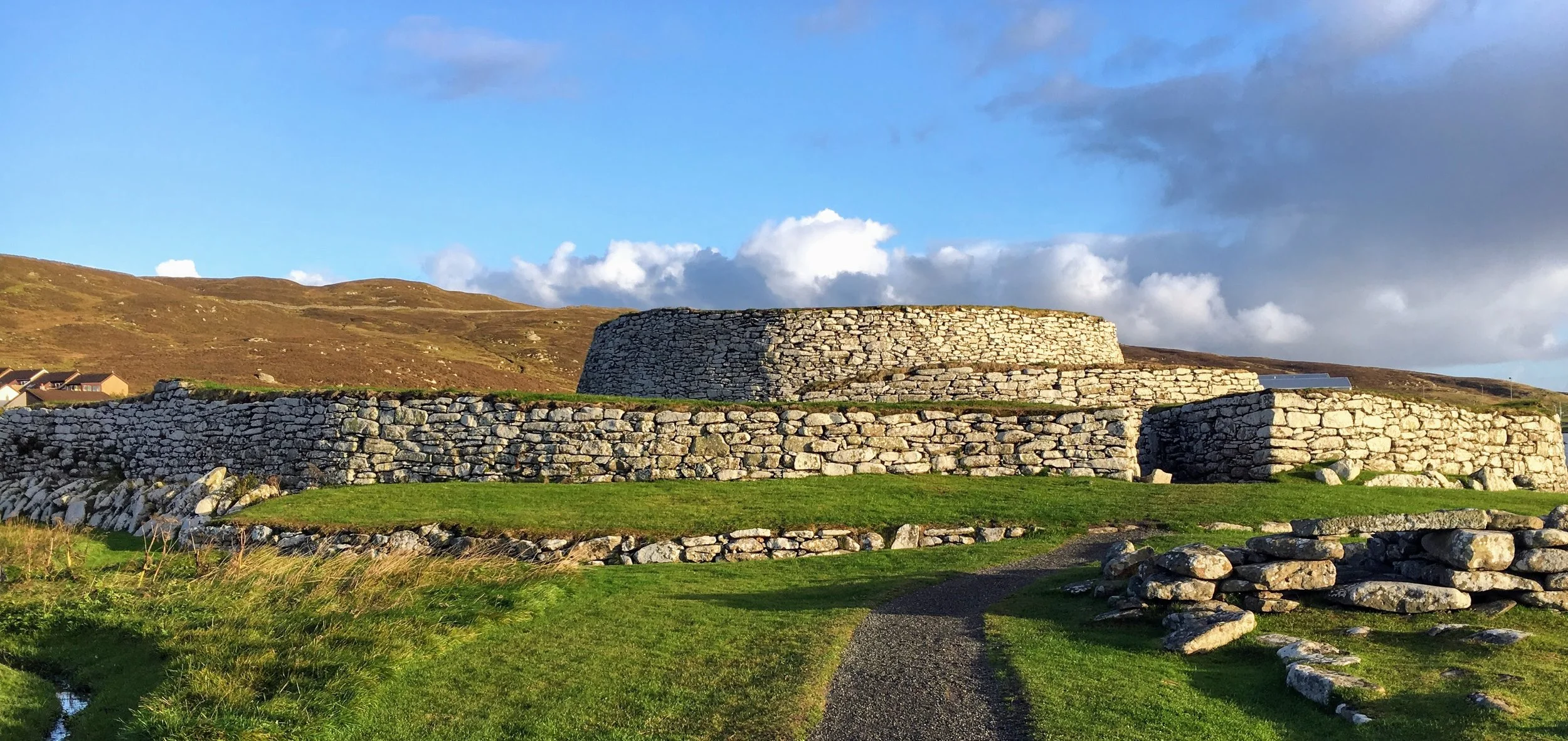 Ancient stone structure on a grassy landscape with hills and blue sky in the background.