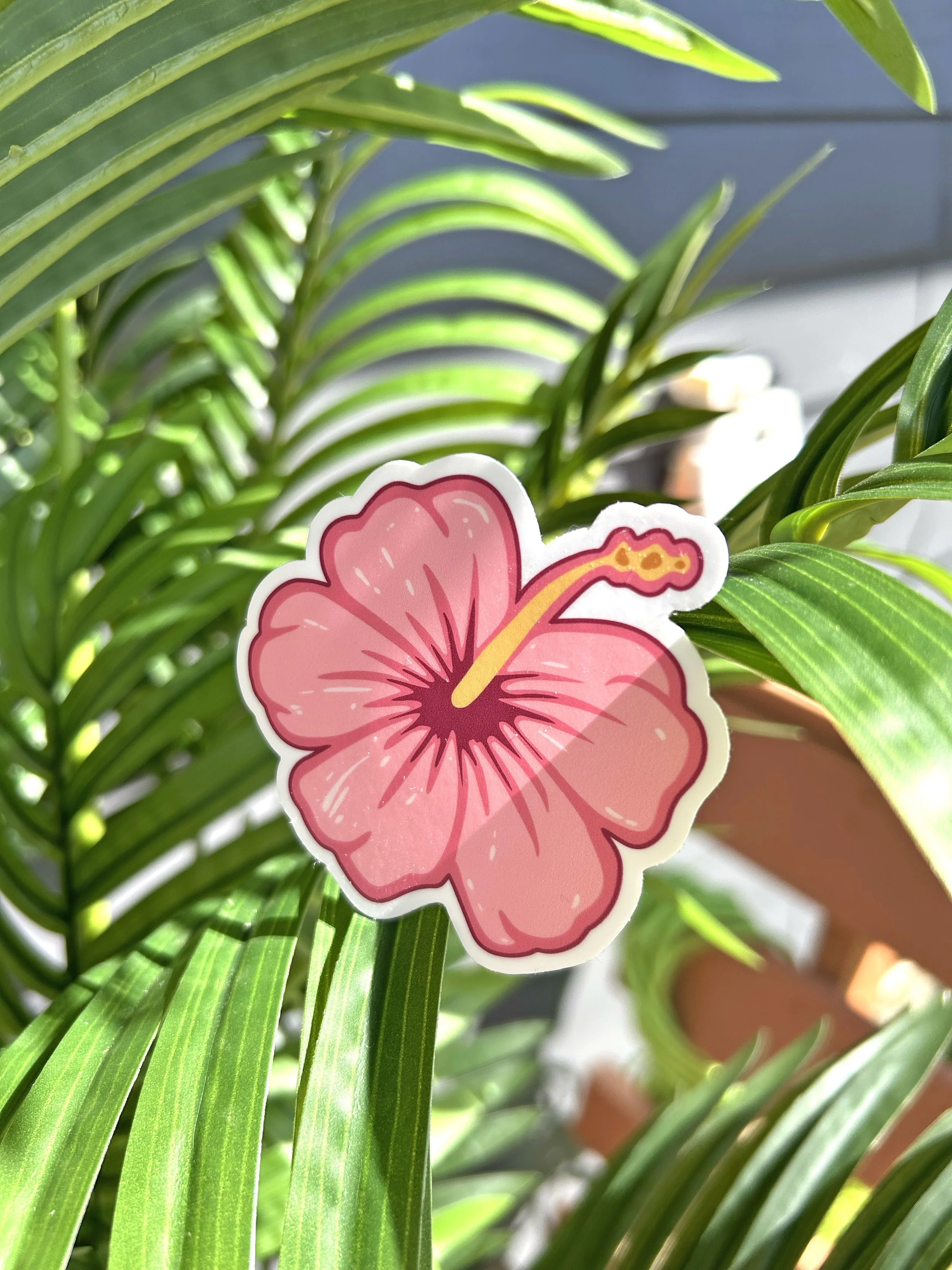 A pink hibiscus flower sticker attached to green plants with long, slender leaves.