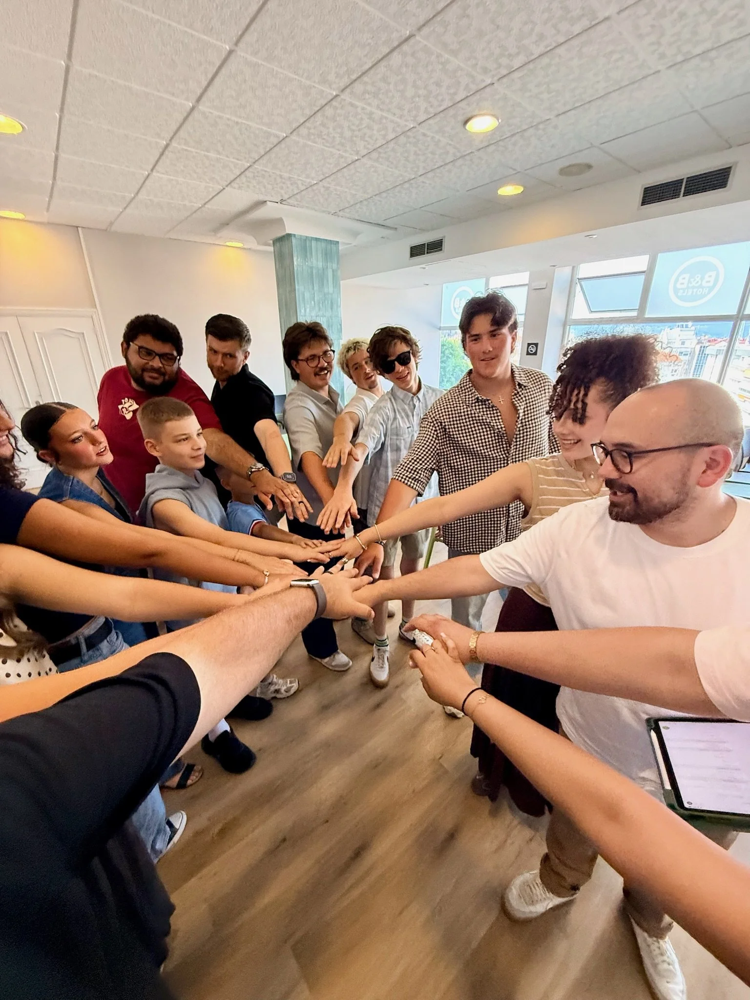 Group of diverse people standing in circle with hands stacked in the center, smiling and engaging in team activity in a bright indoor space in Vigo Spain